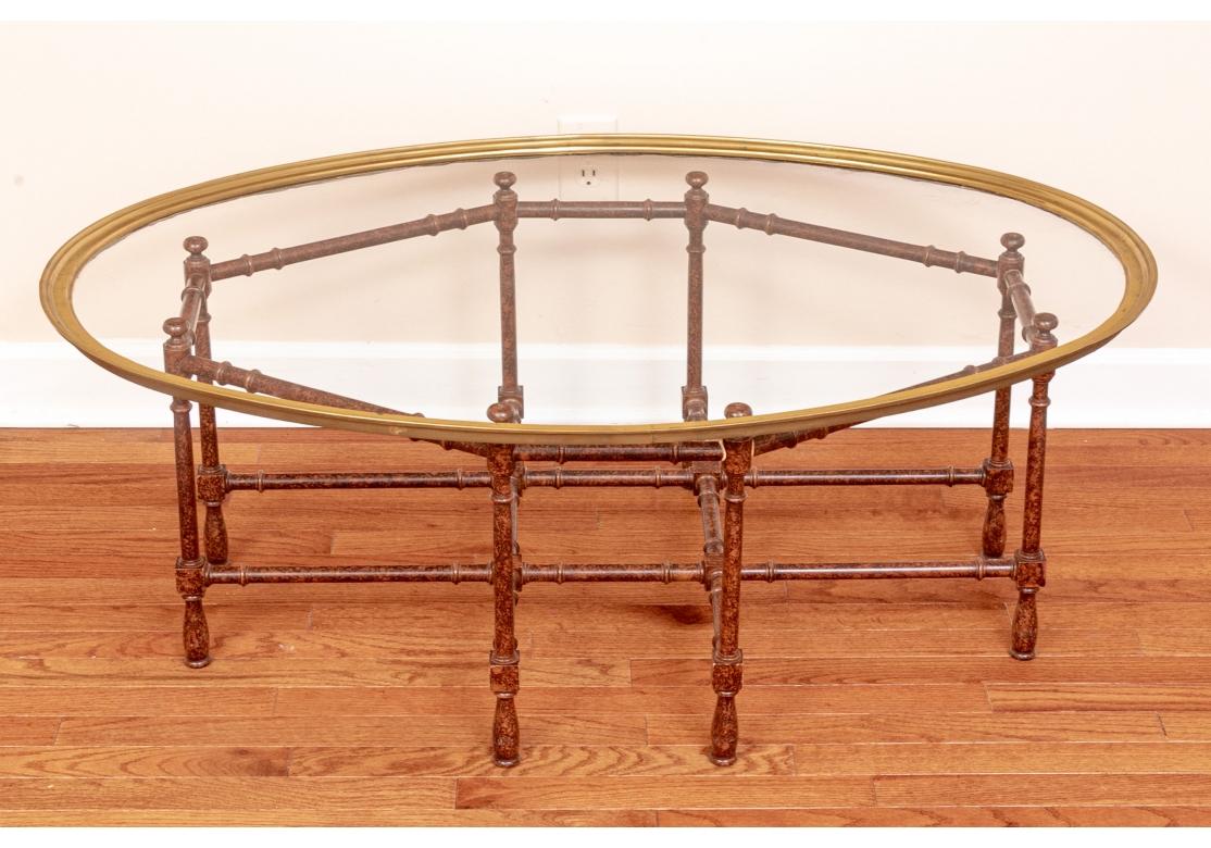 Elegant and light in styling, an Oval Brass Trimmed Glass Top Cocktail Table with a refined air. An oval glass top coffee table with ribbed brass frame on a faux bamboo wood base in a faux tortoise finish. Stretchers along the length and width.

45