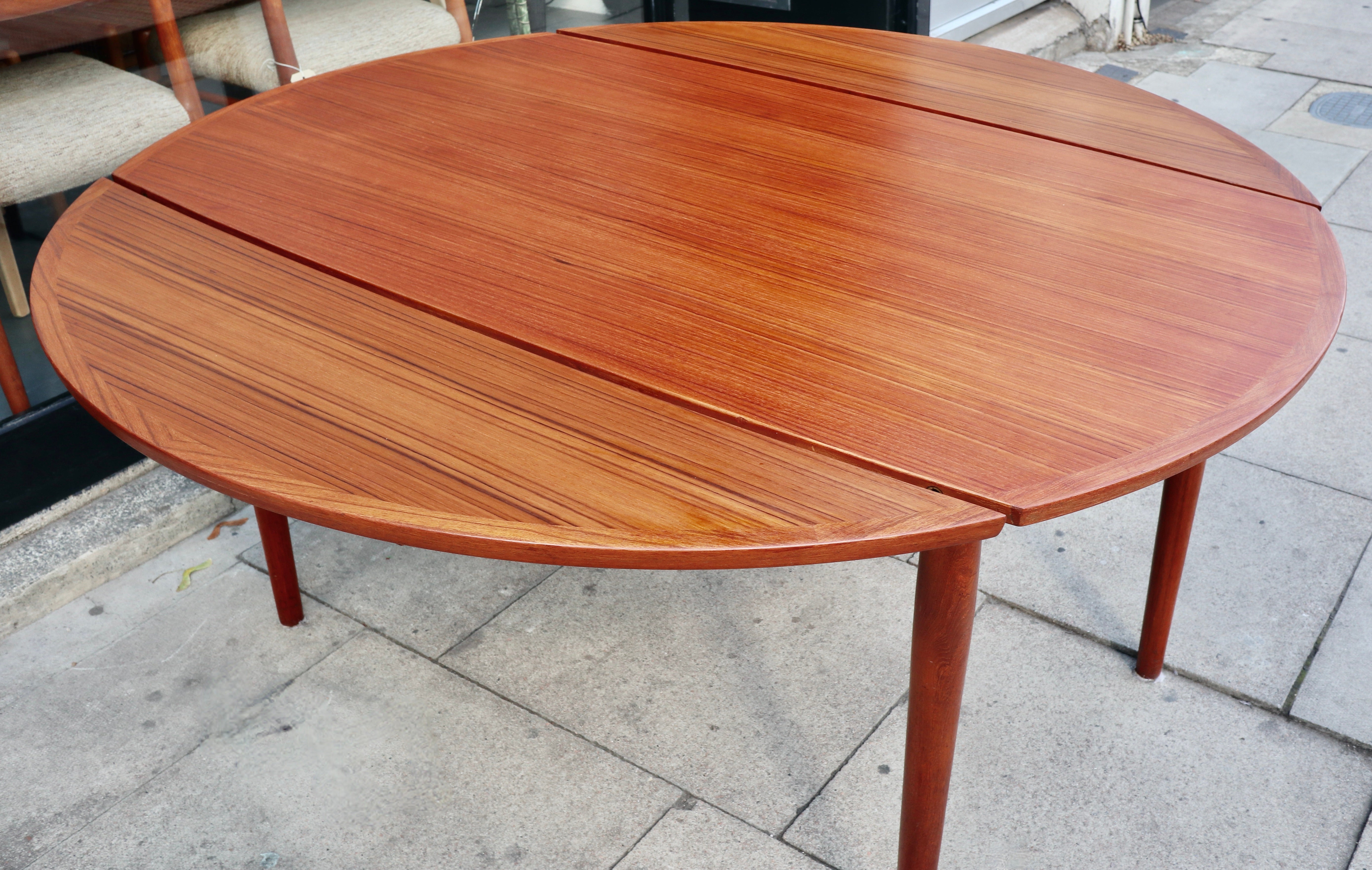 An interesting, unusual and unique 1960s extendable Teak veneered Danish round dining table, designed manufactured by unknown parties.  This table sits on four tapered solid Teak legs, and when unextended, measures 152cm x 85cm, and when fully