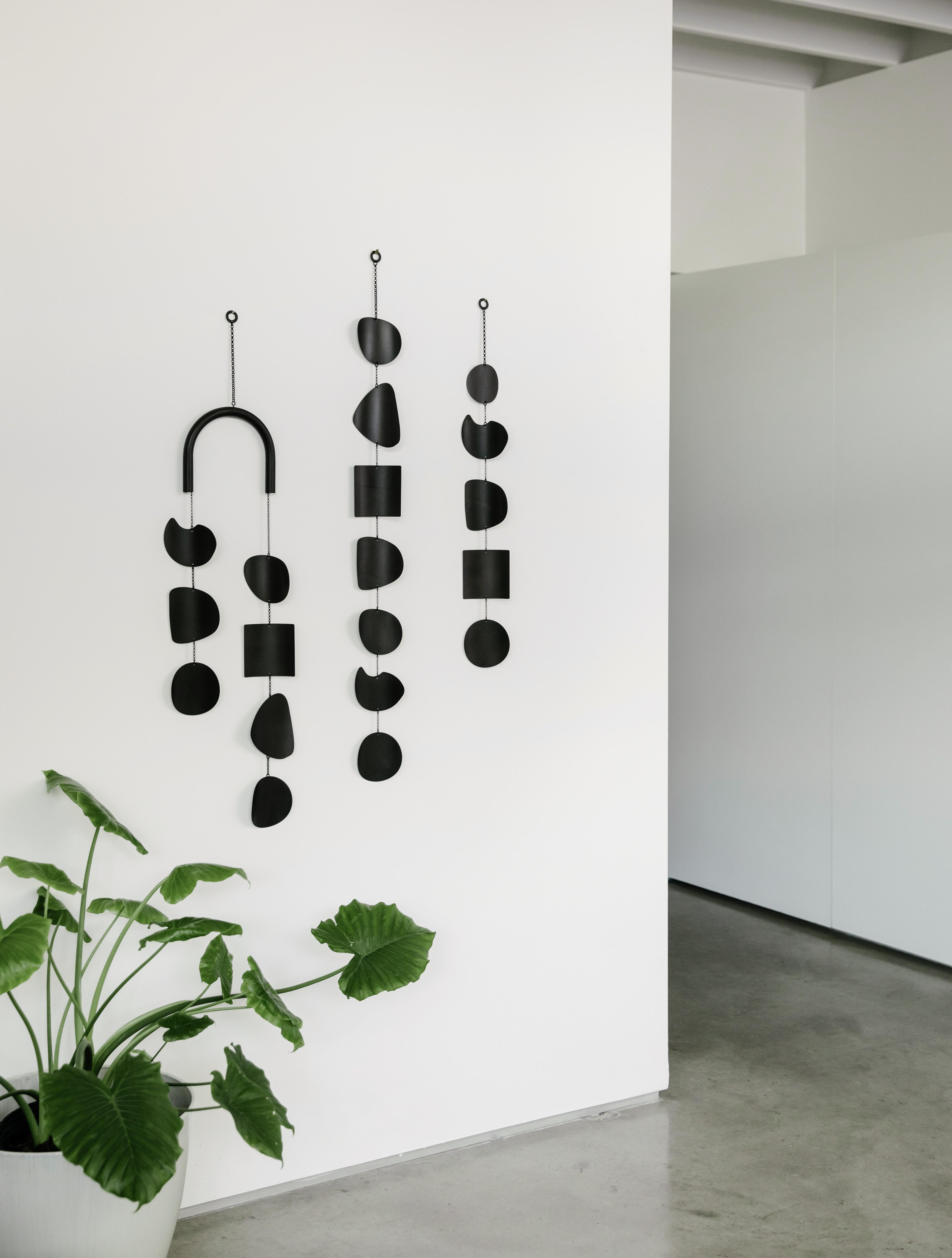 The Quarry Wall Hanging draws inspiration from the worn shapes of river rocks. The curved bar adds a layer of softness and the form of the organic shapes creates inviting dimension, accentuated by the striking black patina finish of this singular