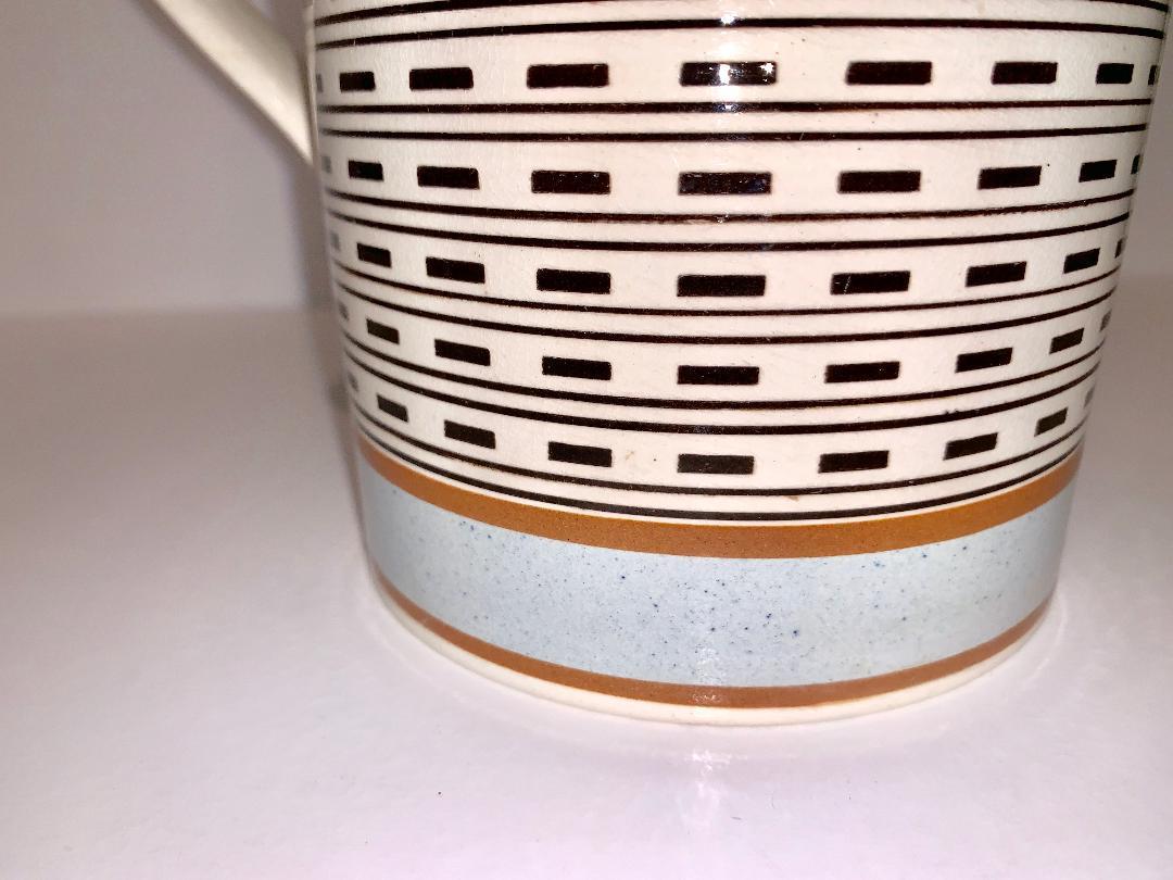 Quart size Mochaware mug. England, circa 1820. A beautiful tall mug, decorated with the engine turning dashes of inlaid black slip, bands of speckled baby blue, and light brown slip.
Dimensions: Diameter 4