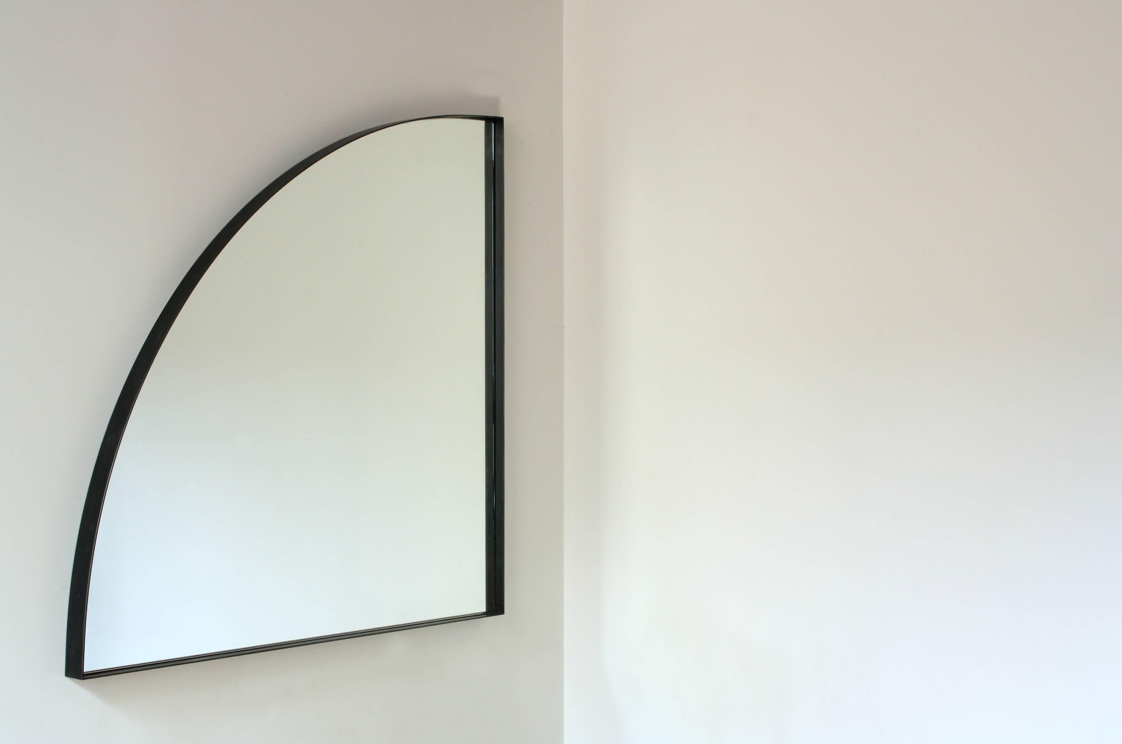 Handmade in Chicago by Laylo Studio, this customizable mirror features a clear, quarter-round mirror with polished edges centered inside a blackened steel frame. A gentle arc connects two points equidistant from the corner matched by the curved edge