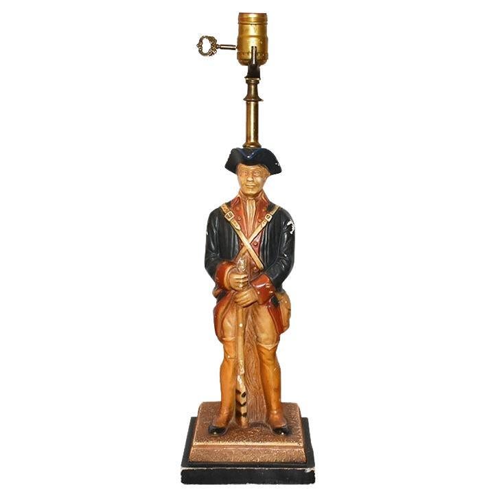 A pair of two Americana table lamps by Quartite Creative Corp. This pair of lamps features two soldiers dressed in their military attire. They wear blue coats, and blue hats and carry rifles. Each perches against a tree stump. The bases are square