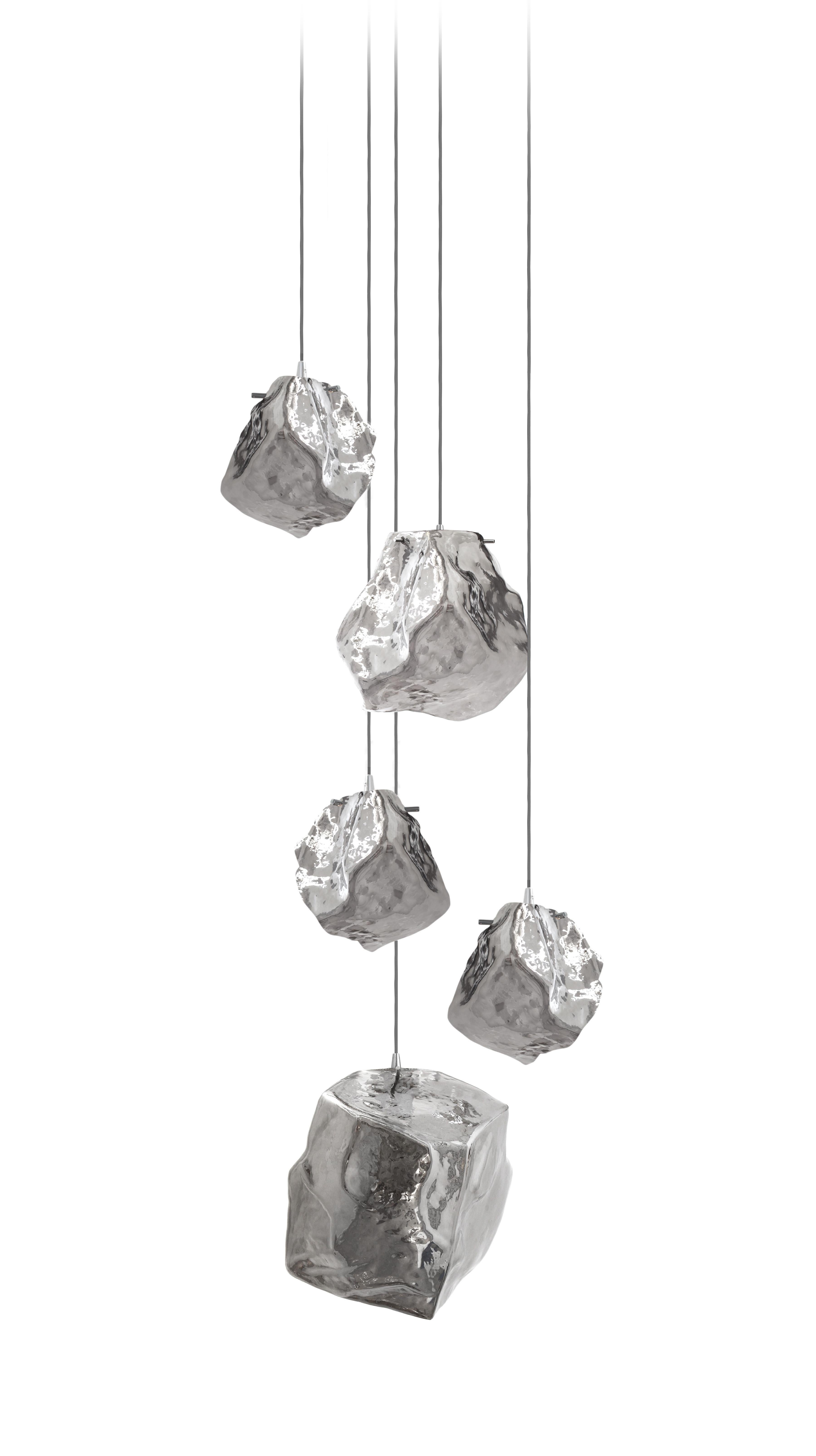 Suspension à 5 lumières en verre Quartz sur un baldaquin de 60 cm.

Ces lunettes moulées à la main ont une surface irrégulière qui leur confère une apparence stellaire et élégante.

Inspirées par les corps célestes qui orbitent dans l'univers, les