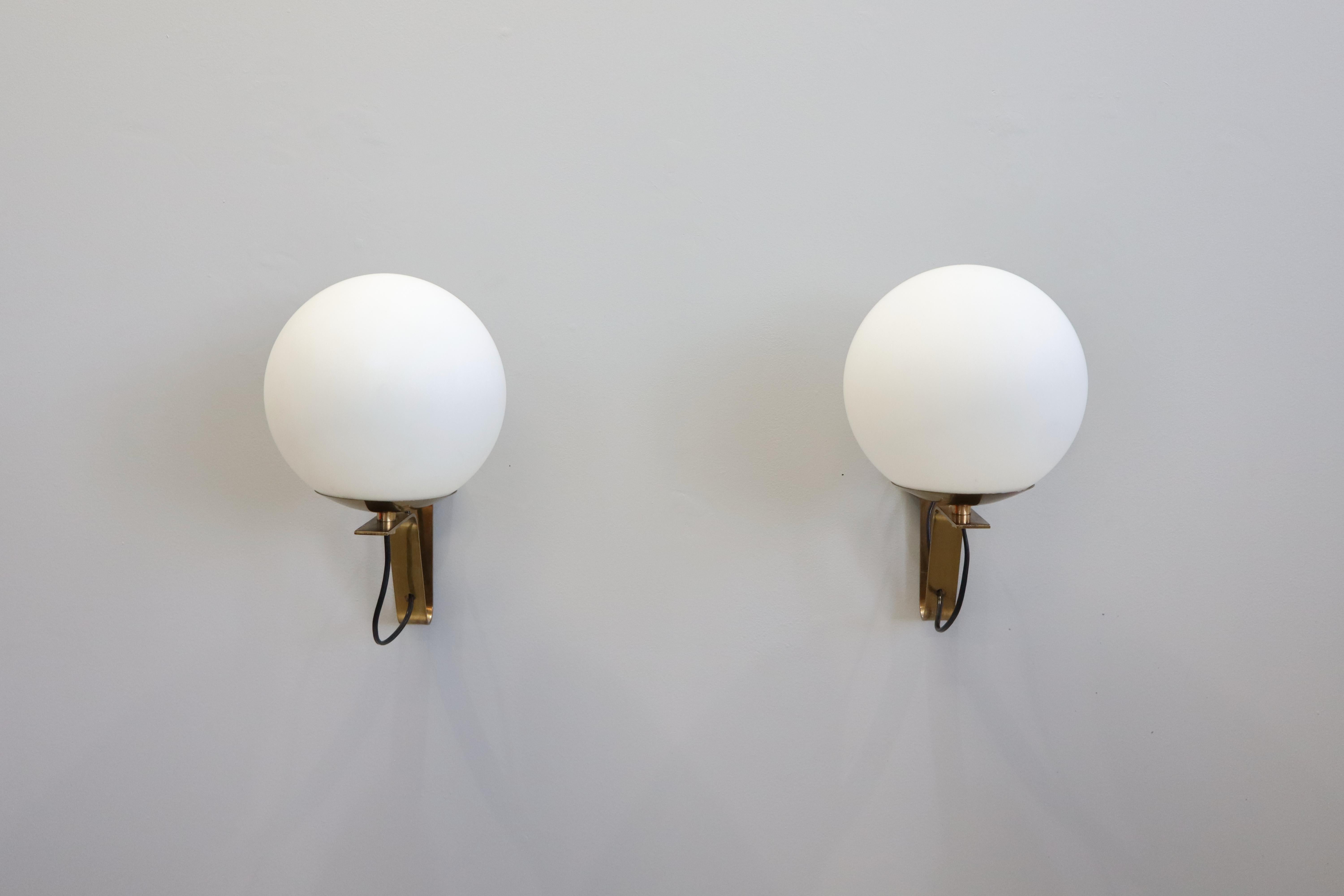 Model b464 sconces by Sergio Asti for Candle. 
Designed and manufactured in Italy circa 1960. 
The sconces are mounted on a polished brass L-shaped bracket that smoothly supports a frosted white globe above the bulb