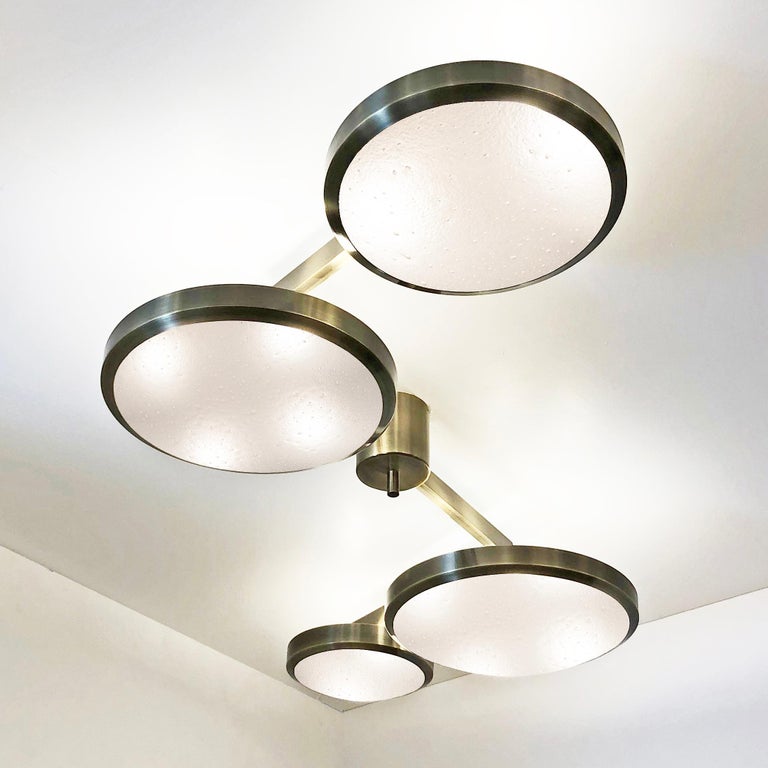 The Quattro ceiling light plays with the notion of lines and shapes, bringing the concept to life with its distinctive winding frame with four variable size shades at staggered heights. Shown as a flush mount in the bronzo ottone finish with our