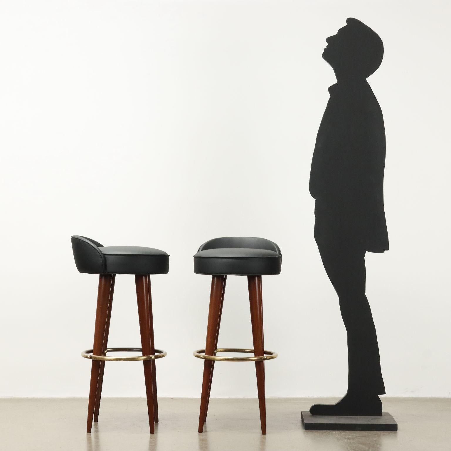 Quattro sgabelli vintage di manifattura italiana con gambe in legno, dettagli in ottone, seduta rivestita in similpelle nera.