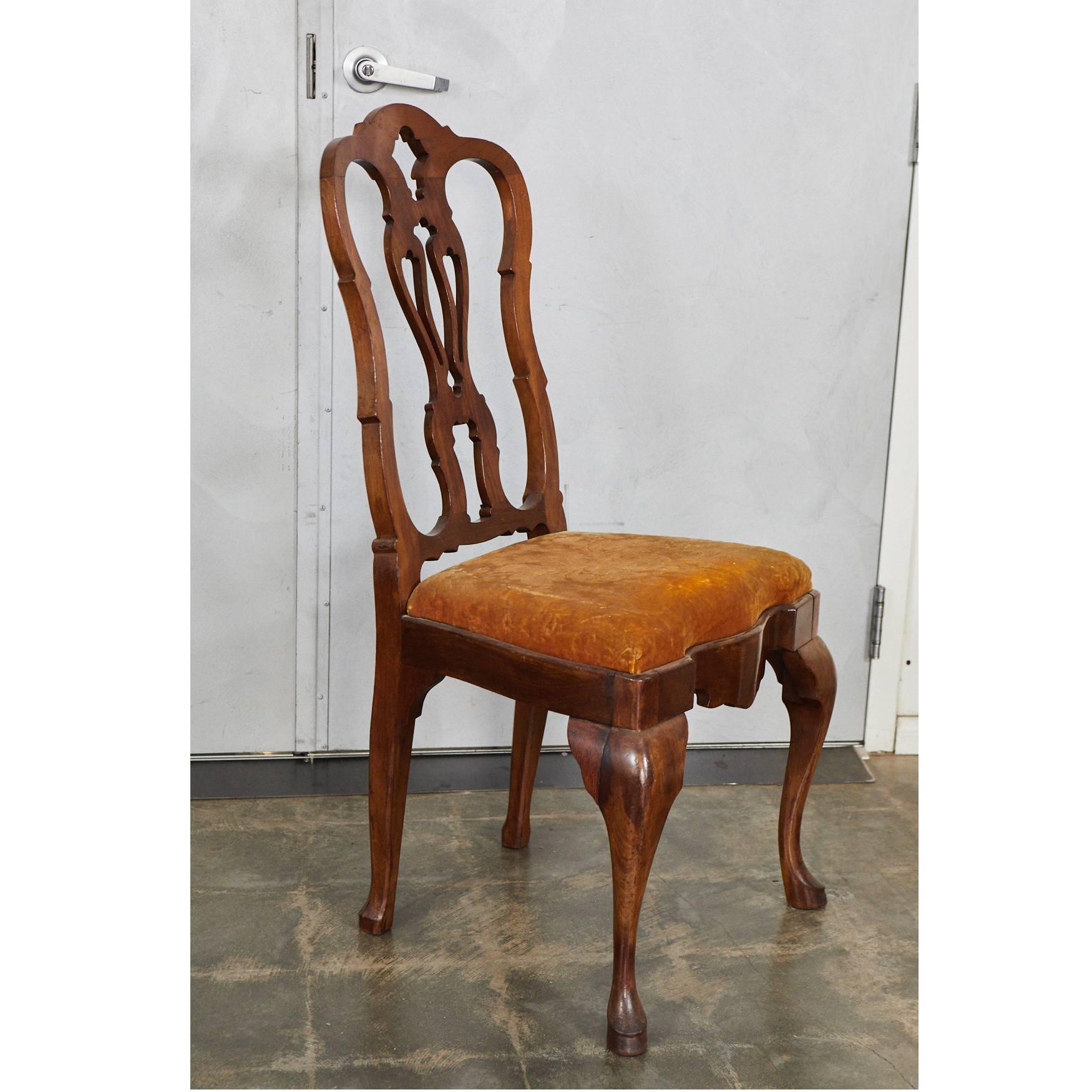 This Queen Ann style side chair is from the 19th century. The chair is made of walnut with decorative elements including a pierced splat along the back and cabriole legs. The seat is upholstered in patterned velvet.

    