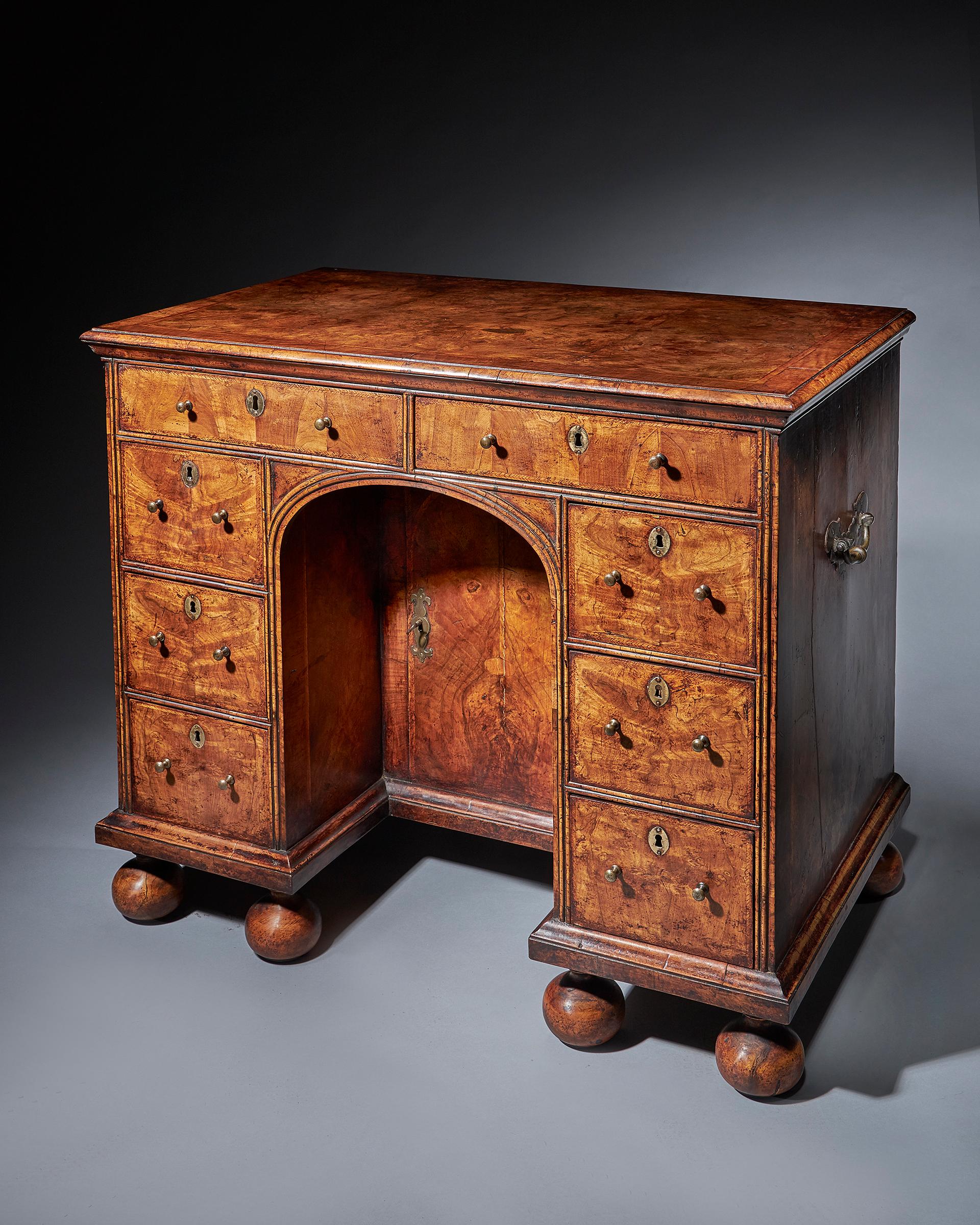 The fine and rare Queen Anne (1702-1714) burr and highly figured walnut kneehole desk.

Above six solid walnut bun feet and cross-grain ogee moulding, six small drawers surround a double dee moulded edged kneehole under two long drawers. The