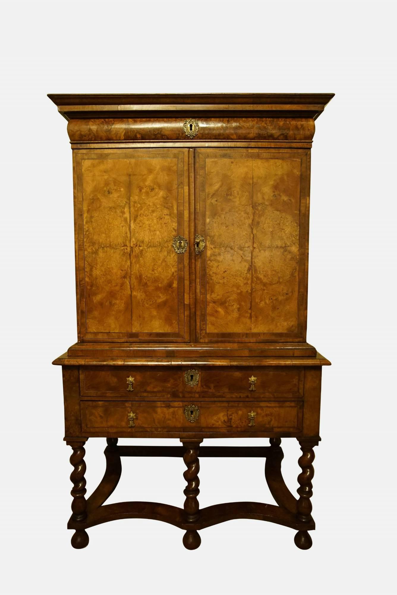 A fine and rare Queen Anne burr walnut cabinet on stand with a frieze drawer above quartered, banded and line inlaid doors opening to an interior of short drawers above the original two drawer base raised on twist turned legs and stretchers (the
