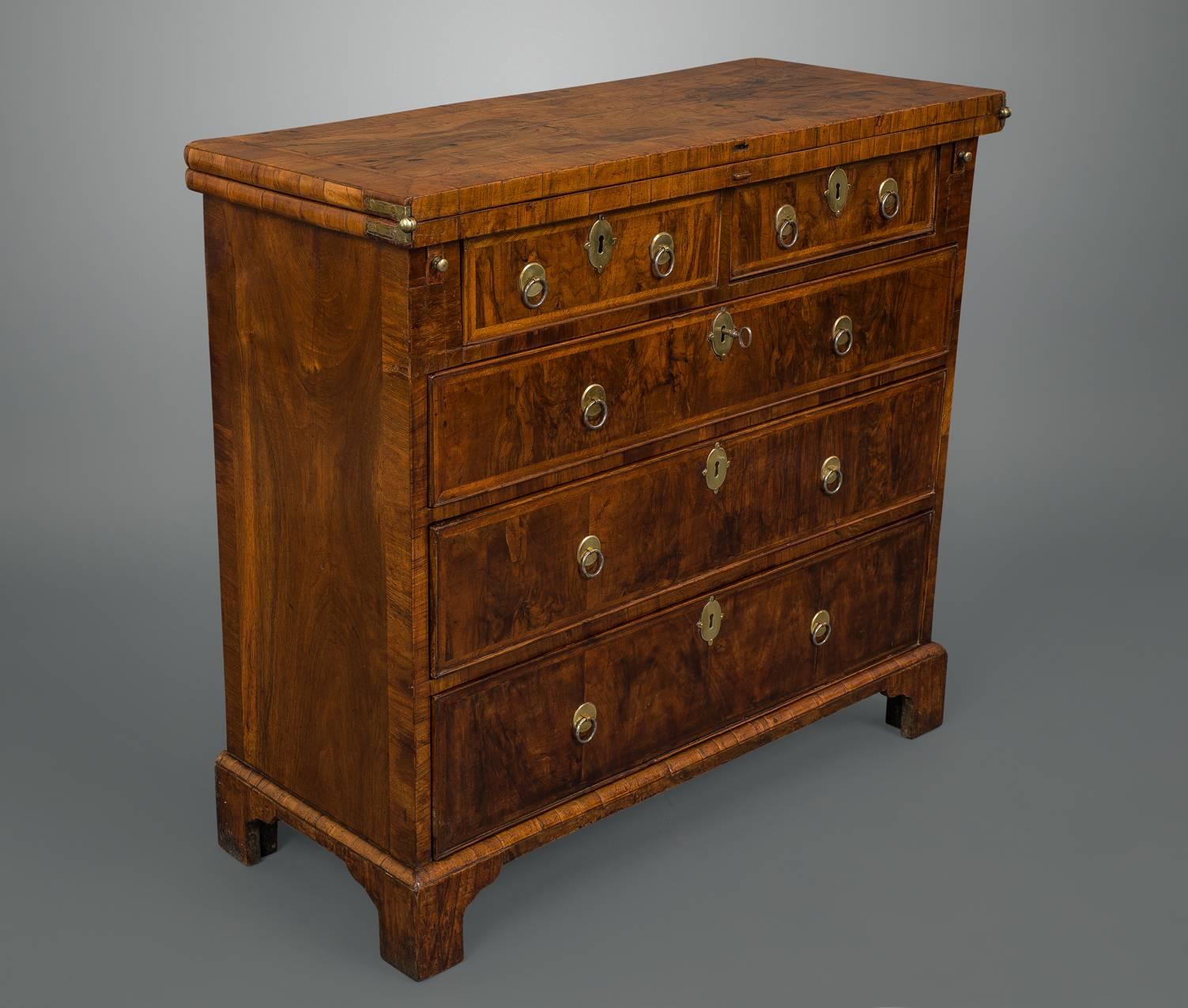 A fine walnut bachelors chest on bracket feet with a wonderful pale toffee color and the added benefit of original ring button handles, escutcheons, locks and hinges.

The top quarter veneered with feather and cross banding exhibiting many