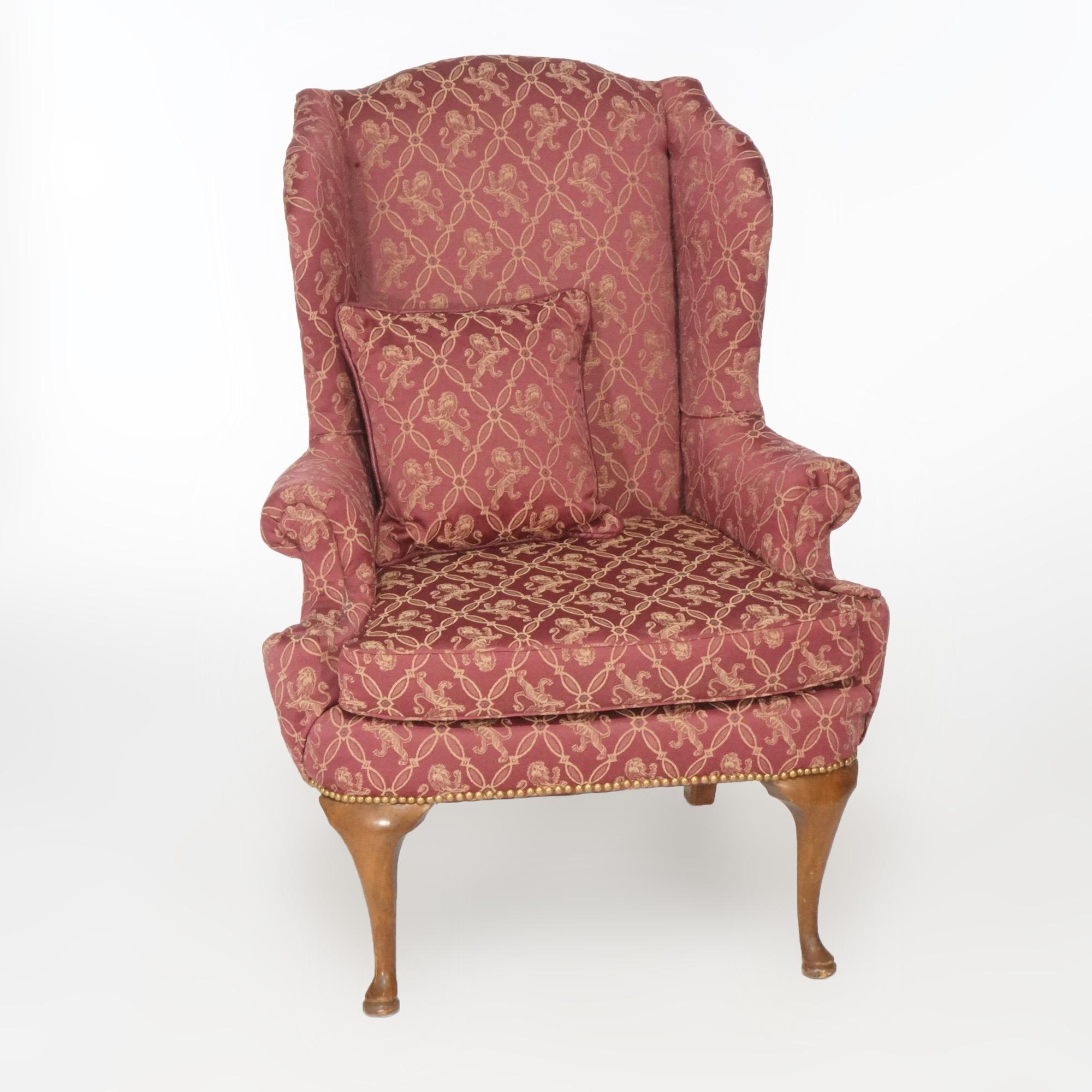 A Queen Anne style fireside wingback chair offers upholstered chair with scroll form arms and raised on mahogany cabriole legs terminating in pad feet, 20th Century.

Measures- 45''H x 32.25''W x 32''D.