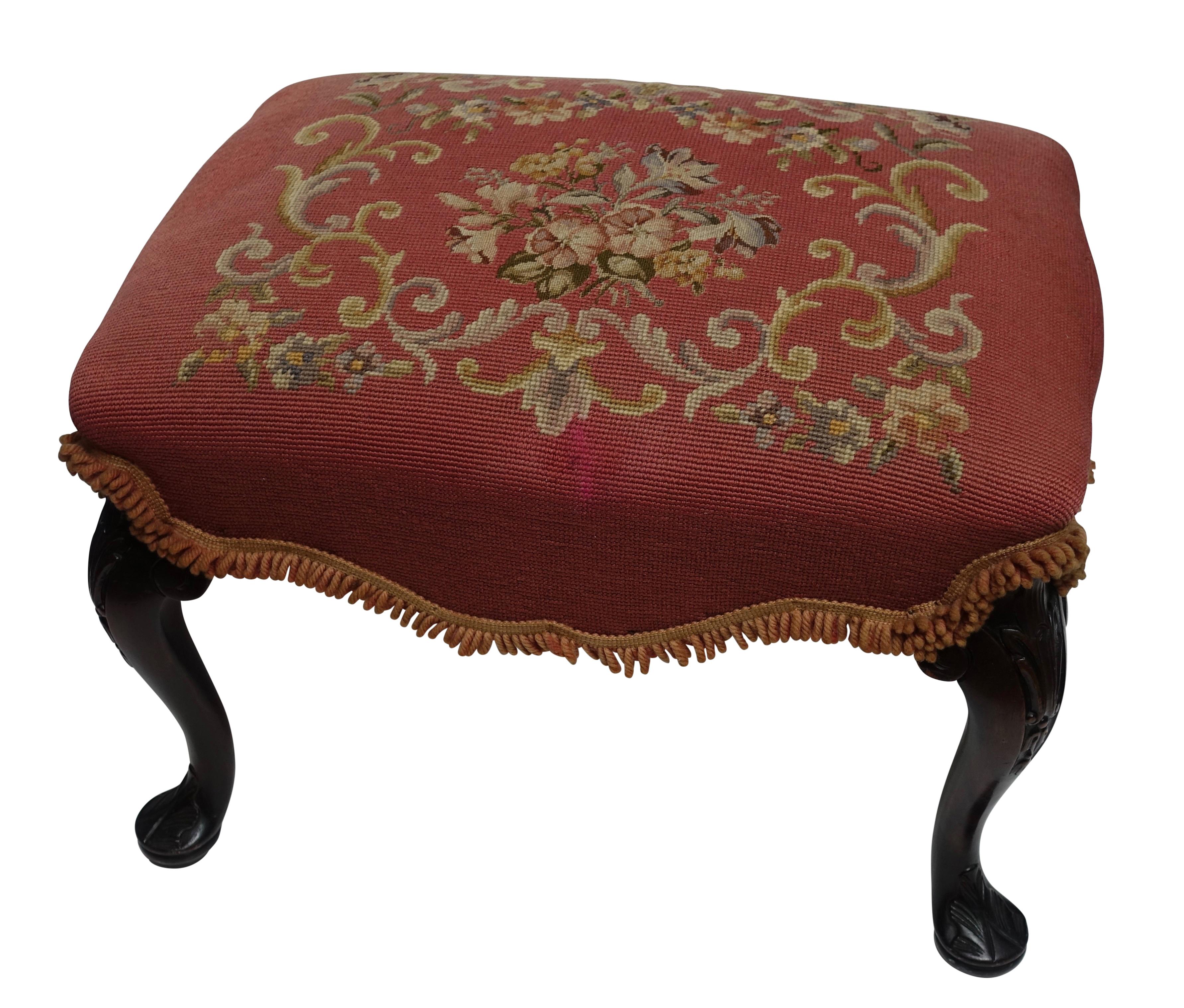 A lovely Queen Anne style mahogany stool with carved cabriole legs ending in carved pad foot, and having a handmade needle point upholstery. American, circa 1920.