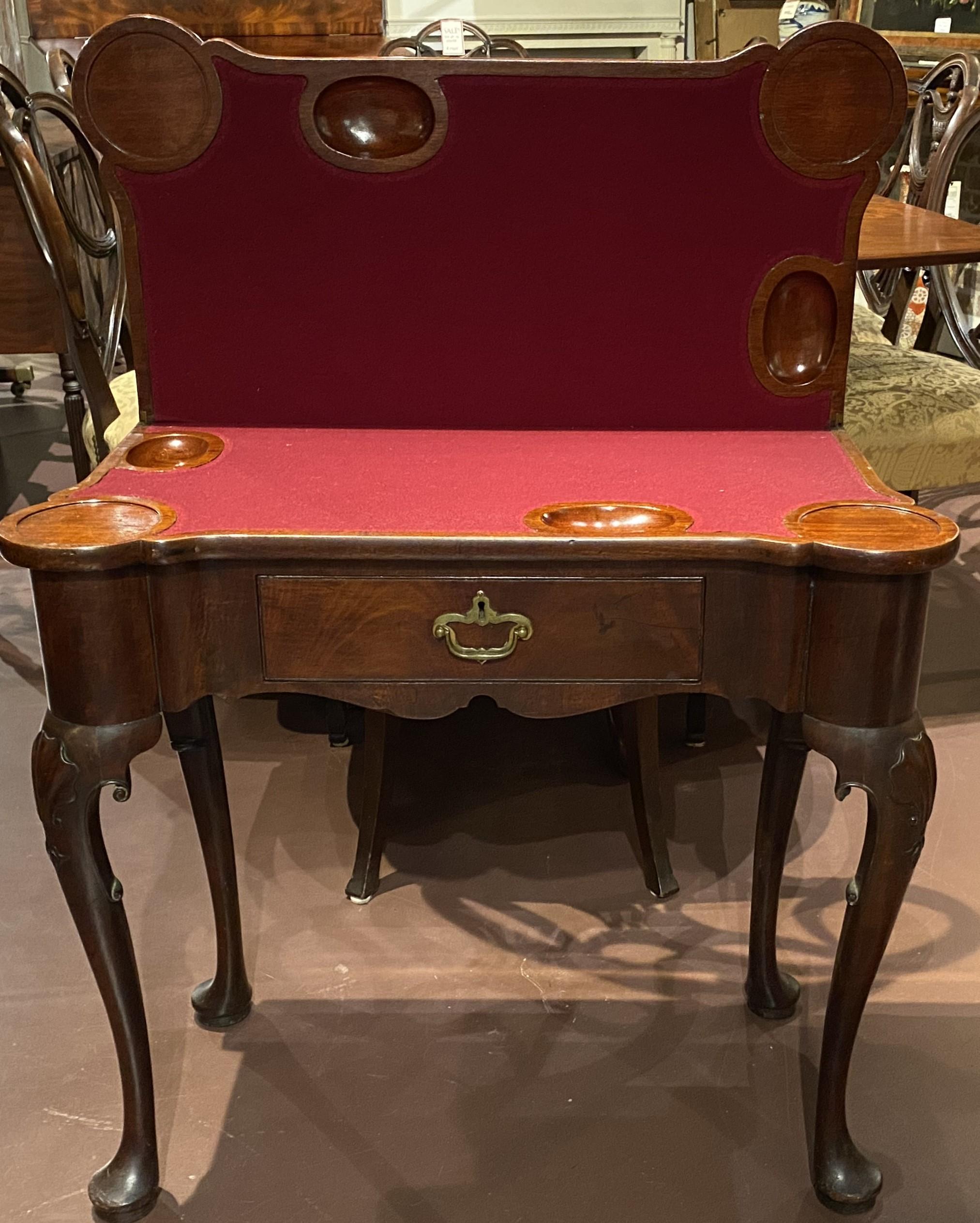 A fine Queen Anne mahogany shell carved card table with single drawer, maroon felt lined and shaped table top with carved wells and corner turrets, and shaped frieze, all supported by shell carved cabriole legs terminating with pad feet. The table