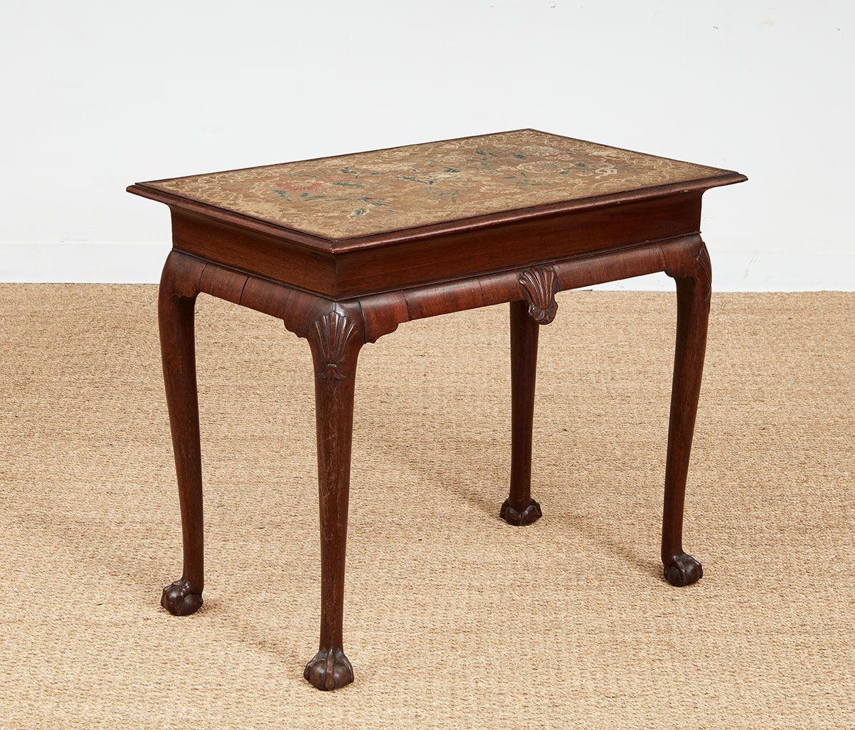 Mesa auxiliar de nogal de la época de la reina Ana, Inglaterra, hacia 1730, que conserva su tablero original de puntada de carpa intrincadamente tejida, con un diseño de tiras alrededor de follaje e inserto en un borde de nogal moldeado.   Centro