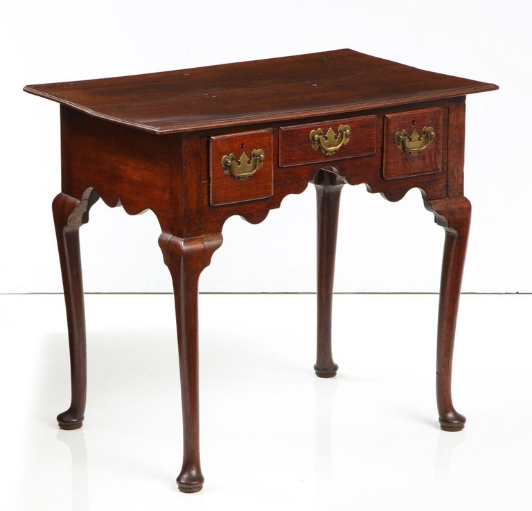 Good early 18th century English oak lowboy, the thumb molded top over two deep and one shallow drawer having original batwing brasses, over a scalloped apron with cupid bow shaped sides and standing on cabriole legs ending in pad feet, the whole