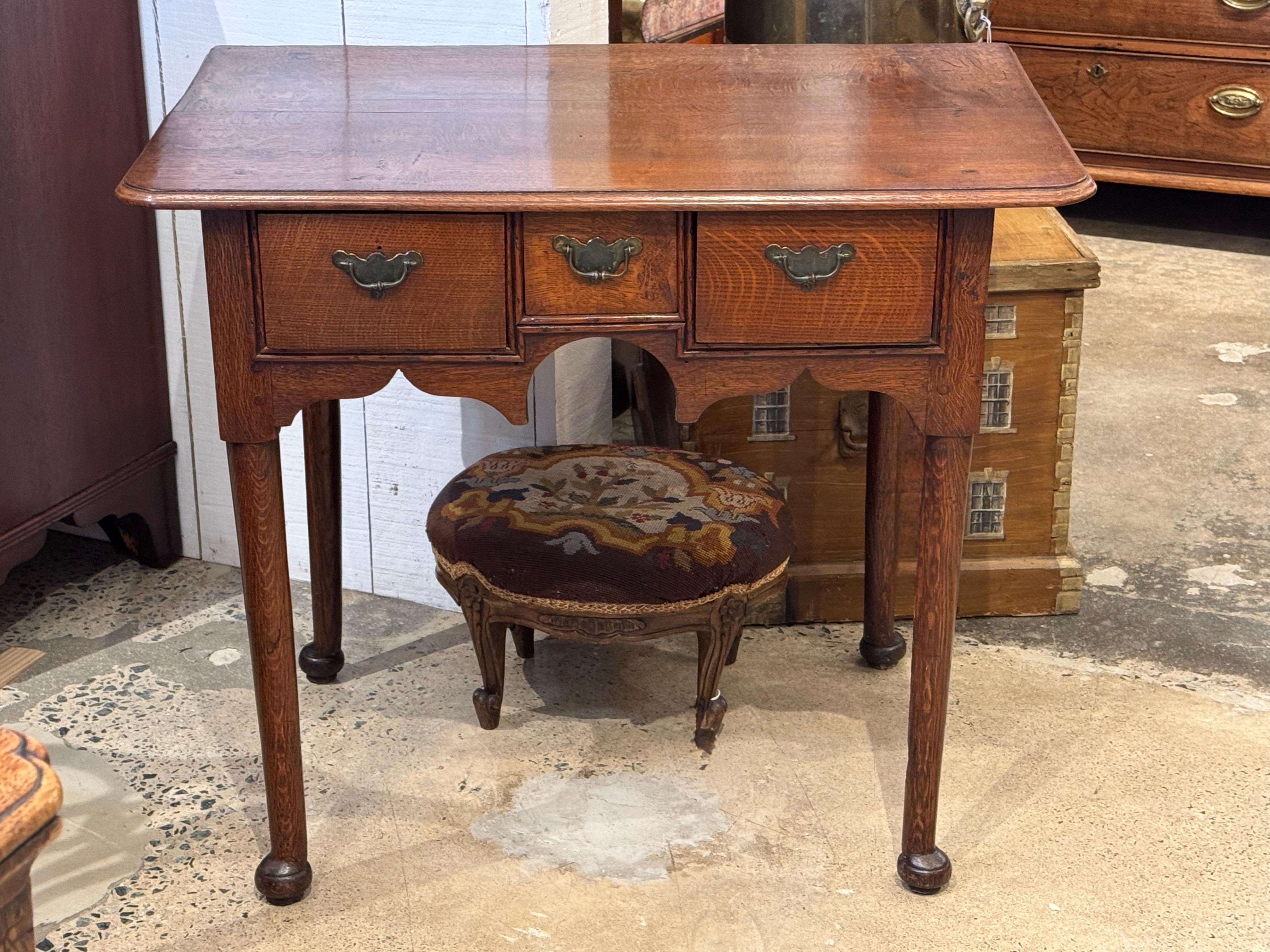 Table d'appoint en chêne avec trois tiroirs et un tablier façonné, soutenue par des pieds pad tournés. Le plateau à une planche est chanfreiné le long du bord et les tiroirs sont dotés de poignées en laiton. Le grain chaud et figuré confère à la