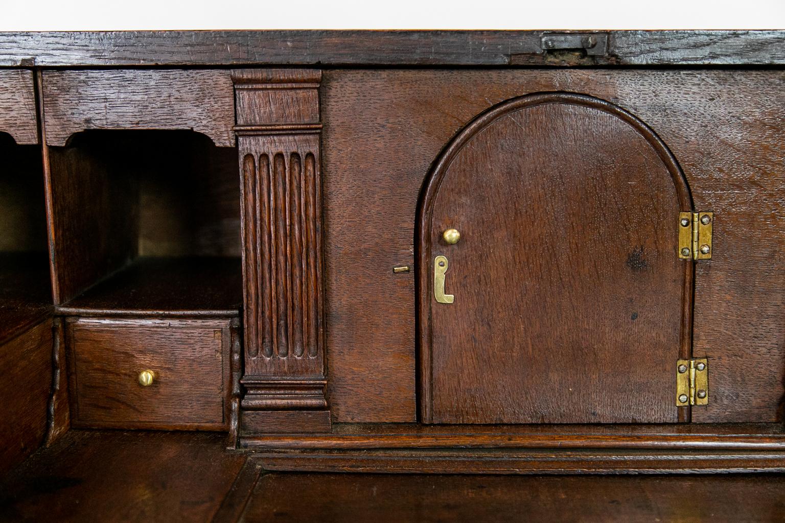 This Queen Anne oak slant front desk has an interior well with a sliding door. There are two very secret compartments behind the two inner drawers, and the fluted pilasters that flank the prospect door pull out to reveal storage compartments. The