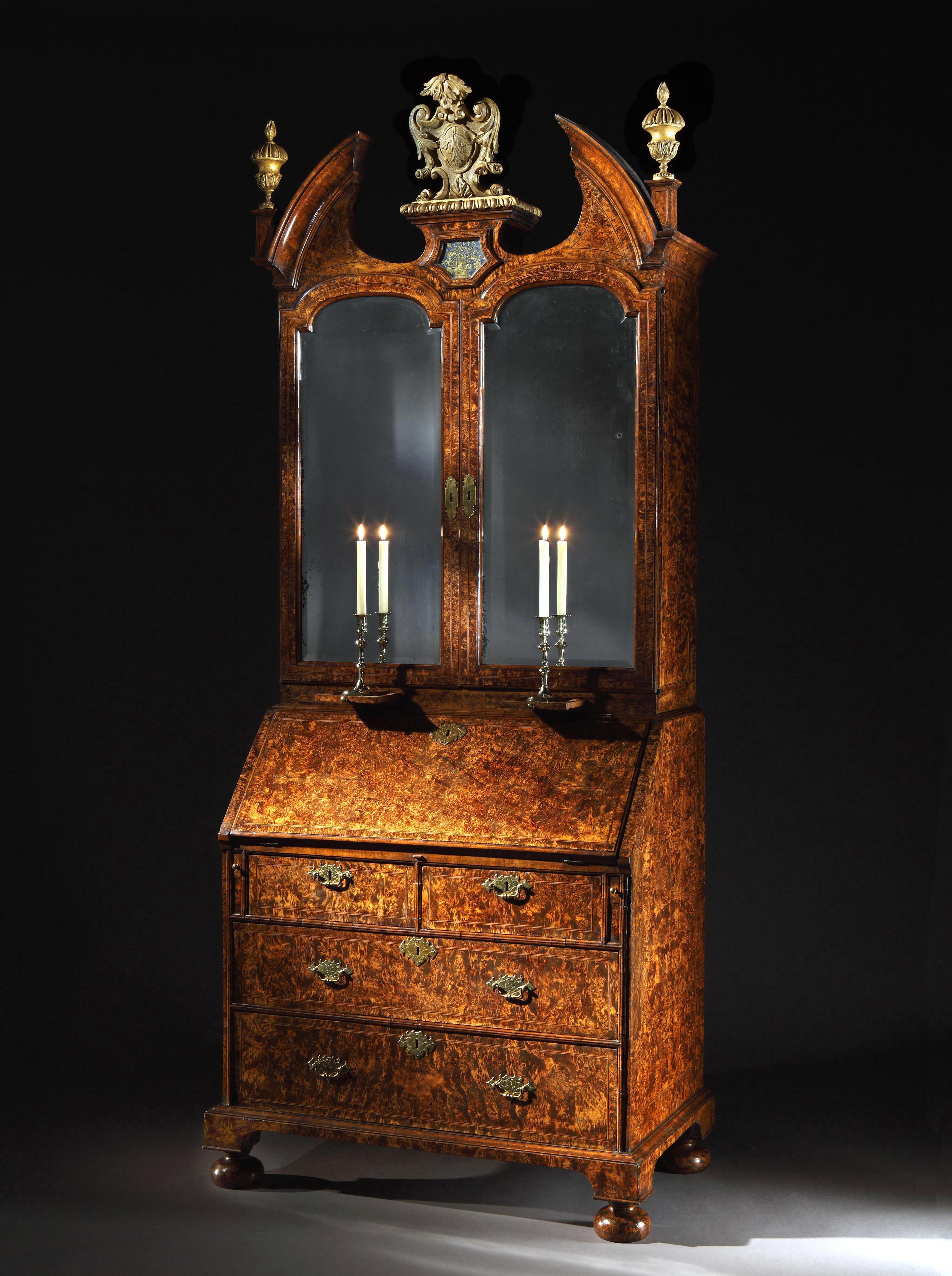 The cabinet with two mirrored doors enclosing an elaborate fitted interior with an arrangement of drawers, cupboard and folio slides; the broken arch pediment centred by a verre églomisé panel with later gilt cartouche and finial; the bureau with