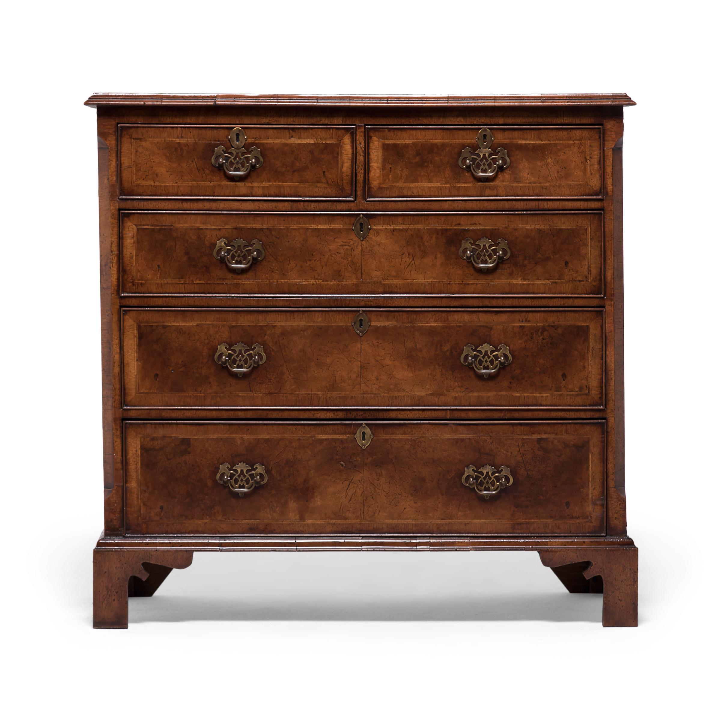 This gorgeous chest of drawers dates to the late-18th century and was crafted in the Queen Anne style with a walnut veneer, bracket feet, and a slightly overhung top. The top is crossbanded with walnut and a thin inset border of contrasting wood.