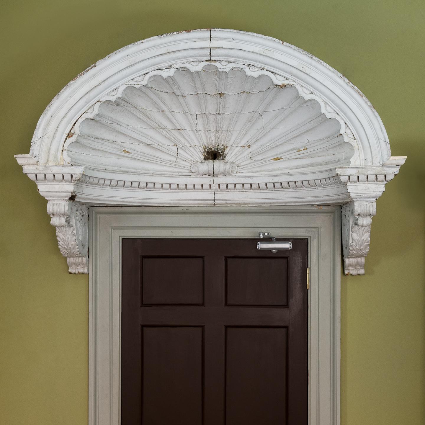 A Queen Anne style shell door hood, late nineteenth century, the carved scallop shell canopy above dentil molding supported on acanthine brackets, painted pinewood.

The internal structure of the piece has been restored and firmed up. There are