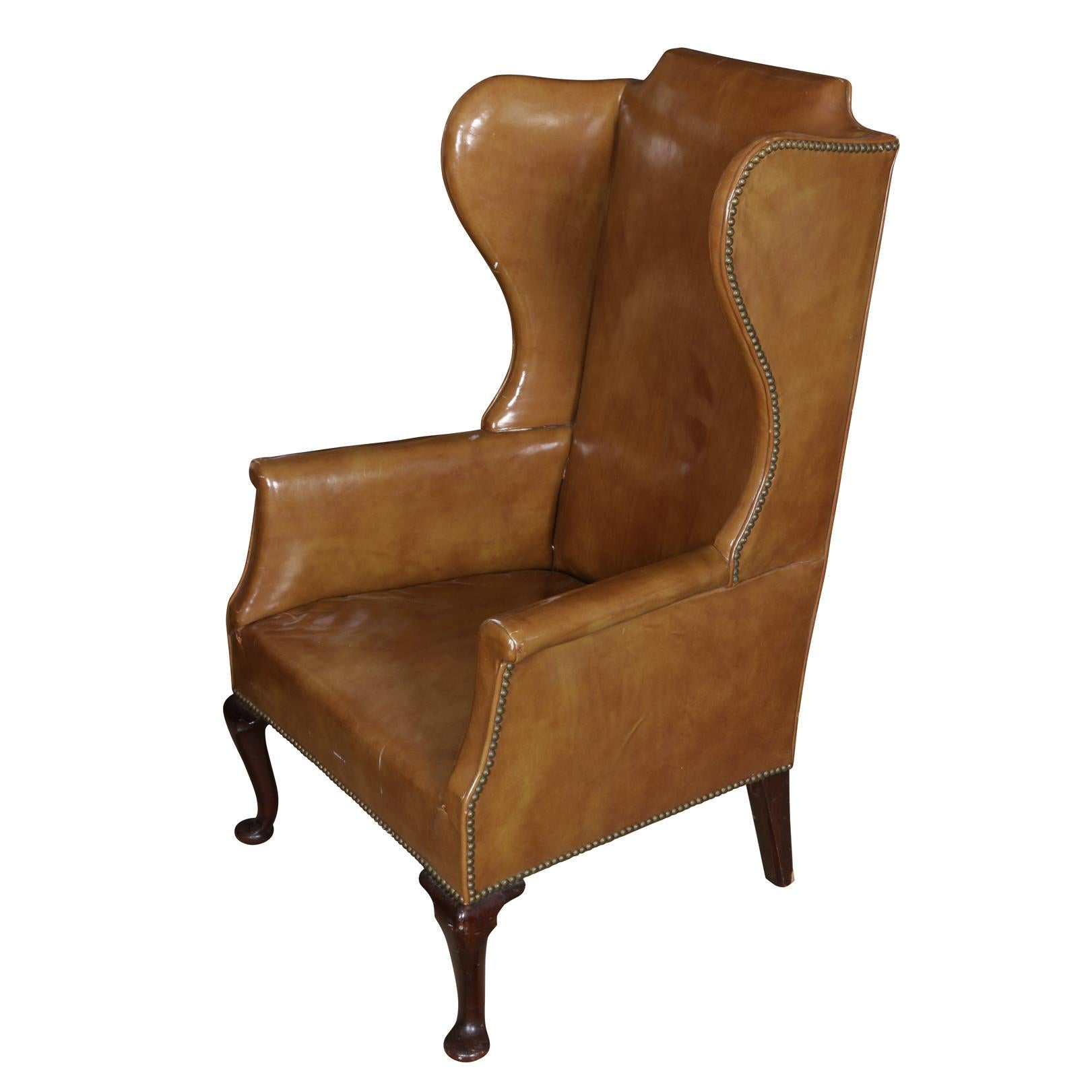 Queen Anne style light brown leather wing chair with nailhead trim, dark wood legs and narrow arms.