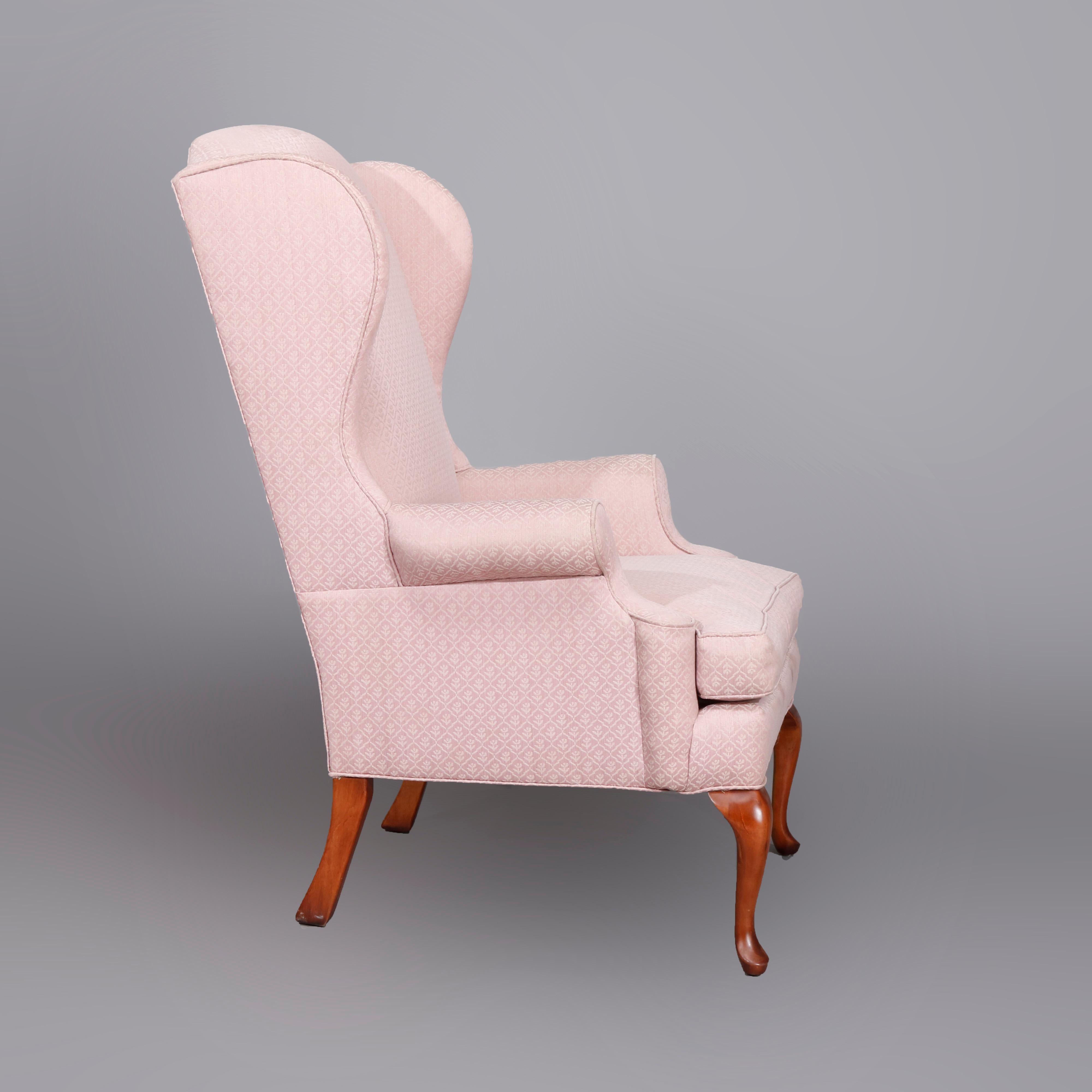 A Queen Anne style wingback chair offers pale pink upholstered chair by Laine Furniture with scroll arms, raised on cabriole mahogany legs, 20th century.

Measures: 45.5