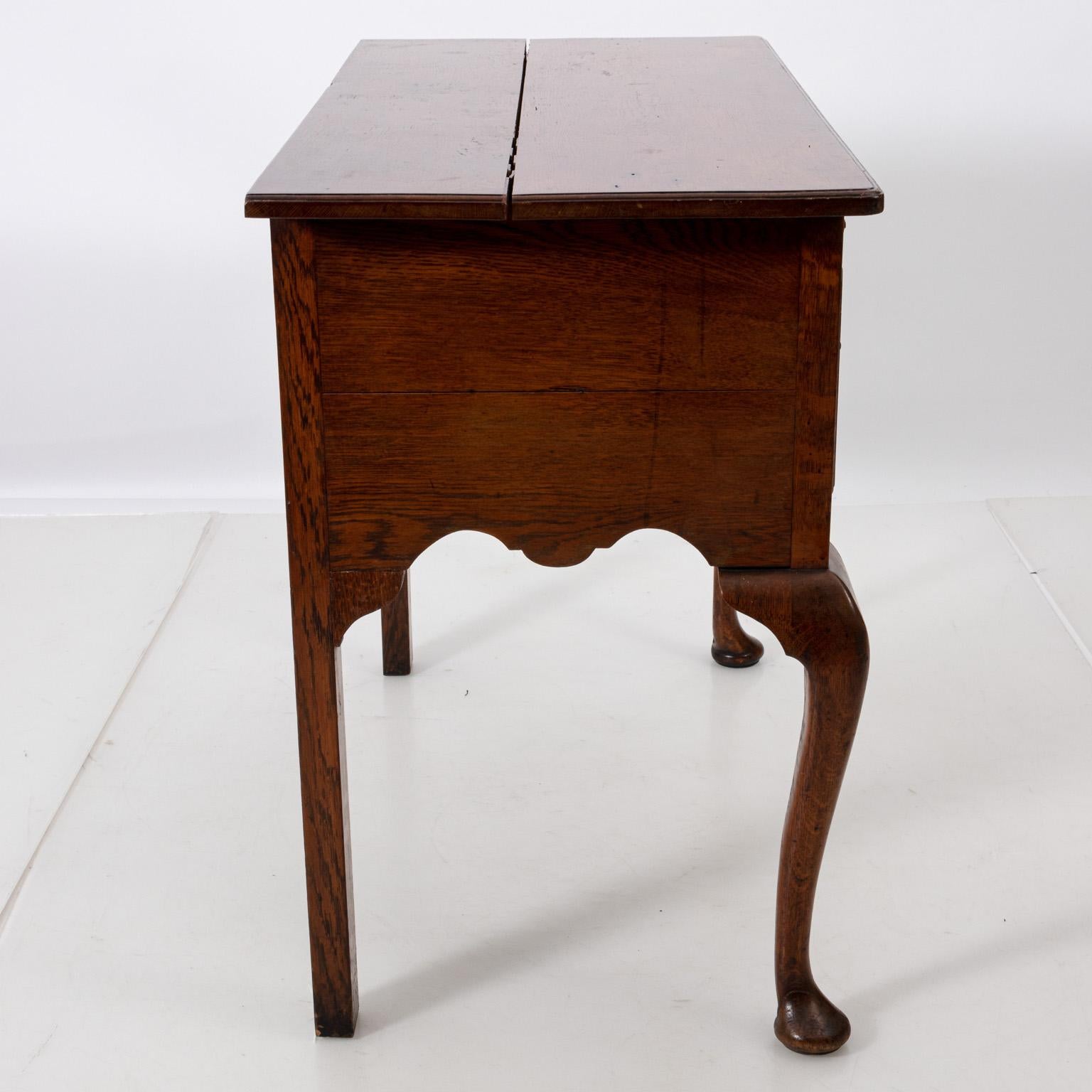 English oakwood low boy in the Queen Anne style with three drawers, cabriole legs, and pad feet, circa 1900s. The piece also features Brass pulls and decorative escutcheon. Please note of wear consistent with age including a split on the tabletop