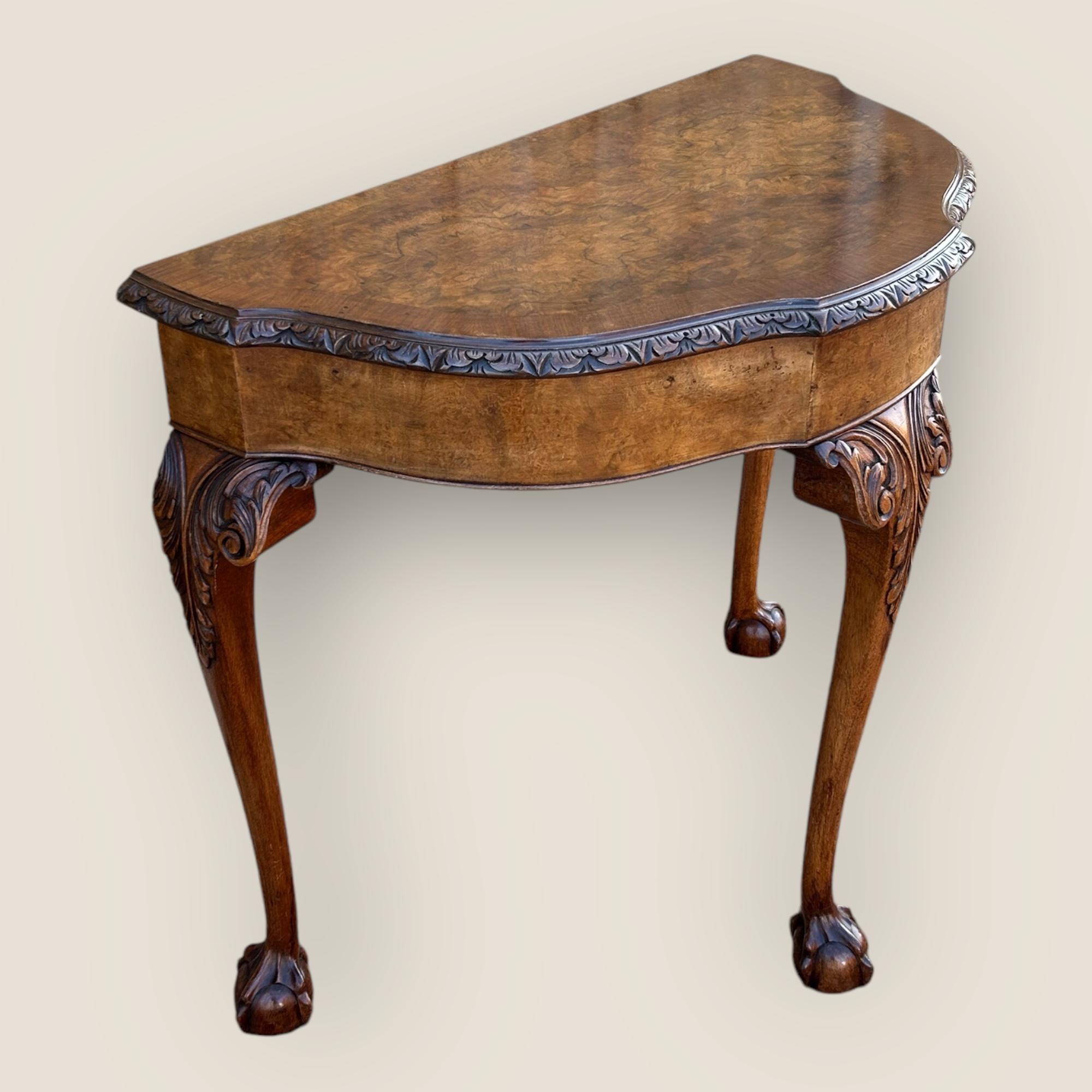 A mid 20th century, circa 1950s/ 1960s, Queen Anne Style Walnut Side Table by Maple & Co. A Demi lune shaped table, with a carved moulding table top edge, 3 carved top cabriole legs, each with ball and claw feet.
