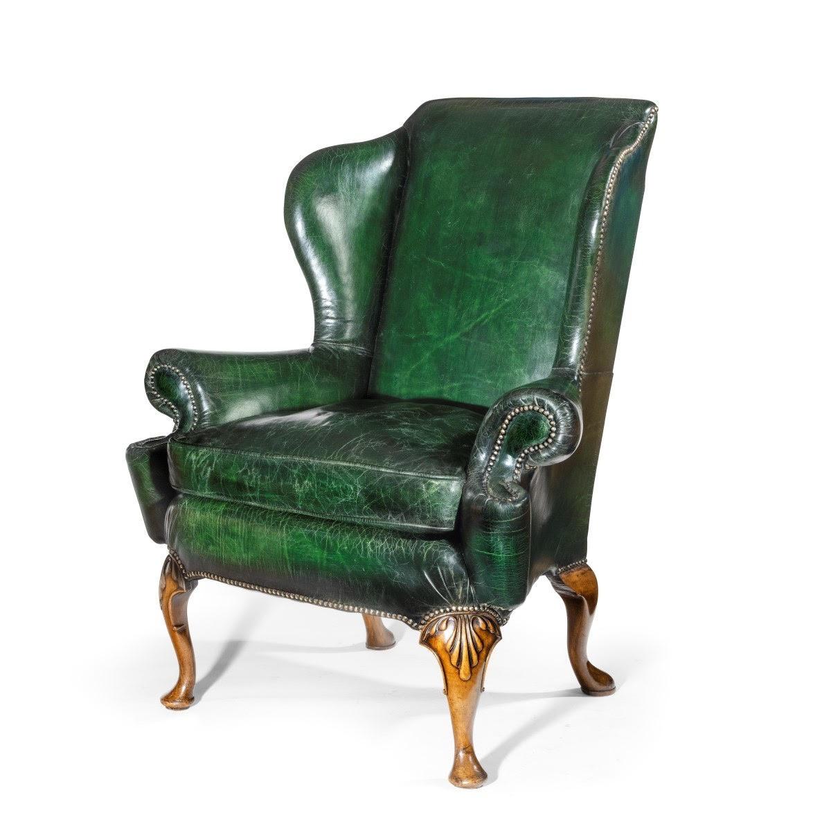 A pair of generous Queen Anne style walnut wing armchairs, of typical form with scrolling arms, fully upholstered, the cabriole legs carved with shells on the knees and terminating in a pad foot.

English, 1920.

Measures: Seat height 23 ½ in.