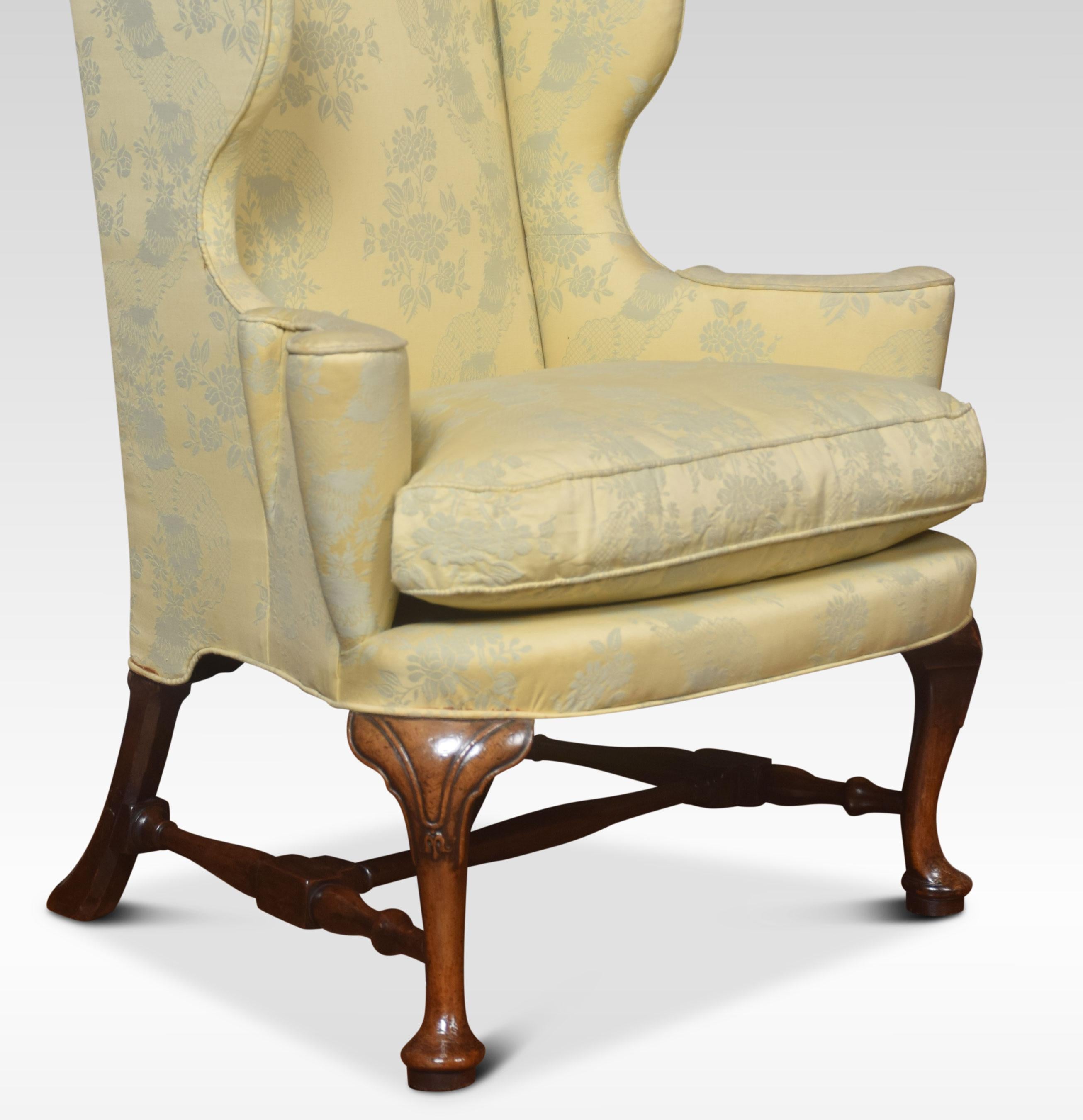 Queen Anne style wing armchair having walnut front carved cabriole legs, with swept legs to the rear united by stretcher. The wing armchair upholstered in damask upholstery having removable cushion.

Dimensions: 

Height 44 inches height to seat