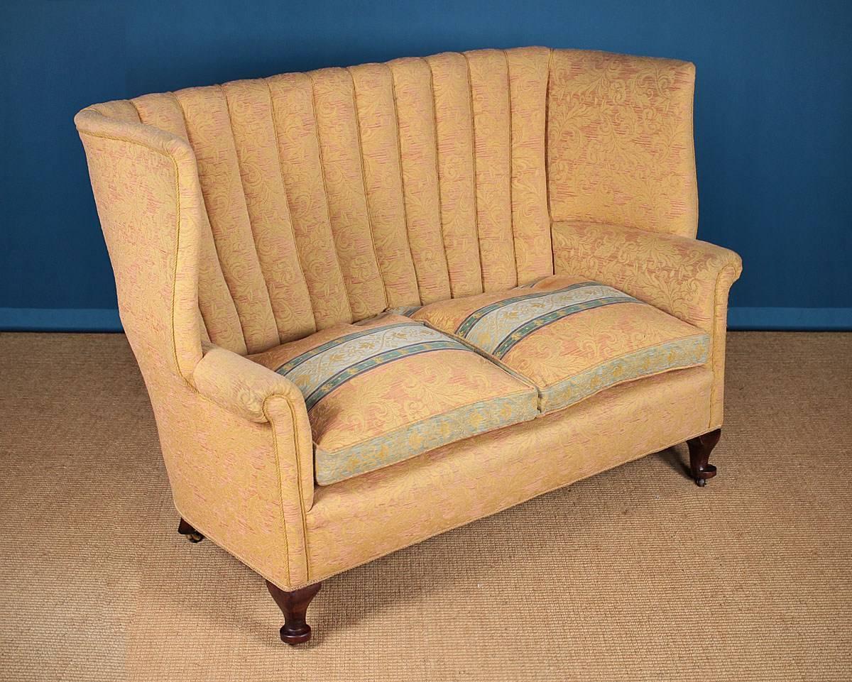 A beautifully elegant Queen Anne style settee or sofa, circa 1920. Having a high backrest with ribbed upholstery with nicely swept wings standing over scroll-top arms. The sprung seat has loose feather filled seat cushions. Raised on short walnut