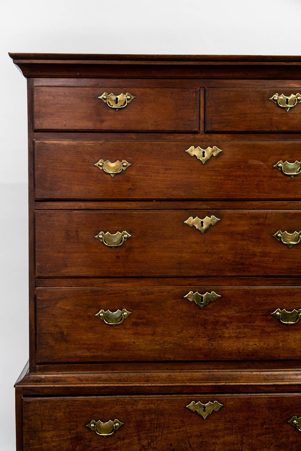 This English highboy is in its original condition including the brasses and finish. The drawers have thumb nail moldings. The lower section has a scalloped apron that joins cabriole legs terminating in pad feet.