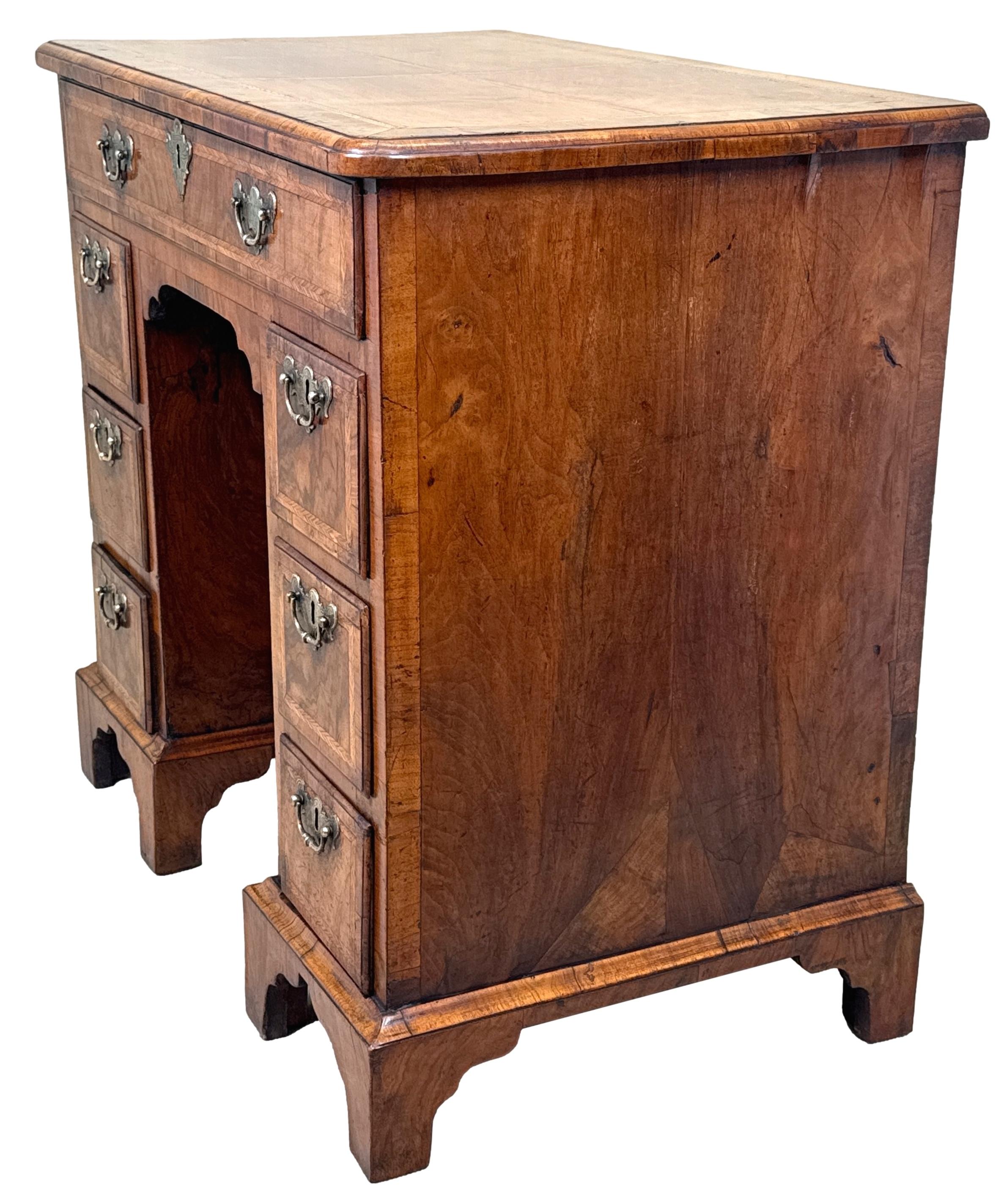 A Charming Early 18th Century Walnut Queen Anne Period Kneehole Desk, Or Dressing Table, Having Superb Quarter Veneered Top, Unusually With Herringbone Inlaid Dividing Panels, Over Arrangement Of Drawers And Central Recessed Cupboard, Retaining