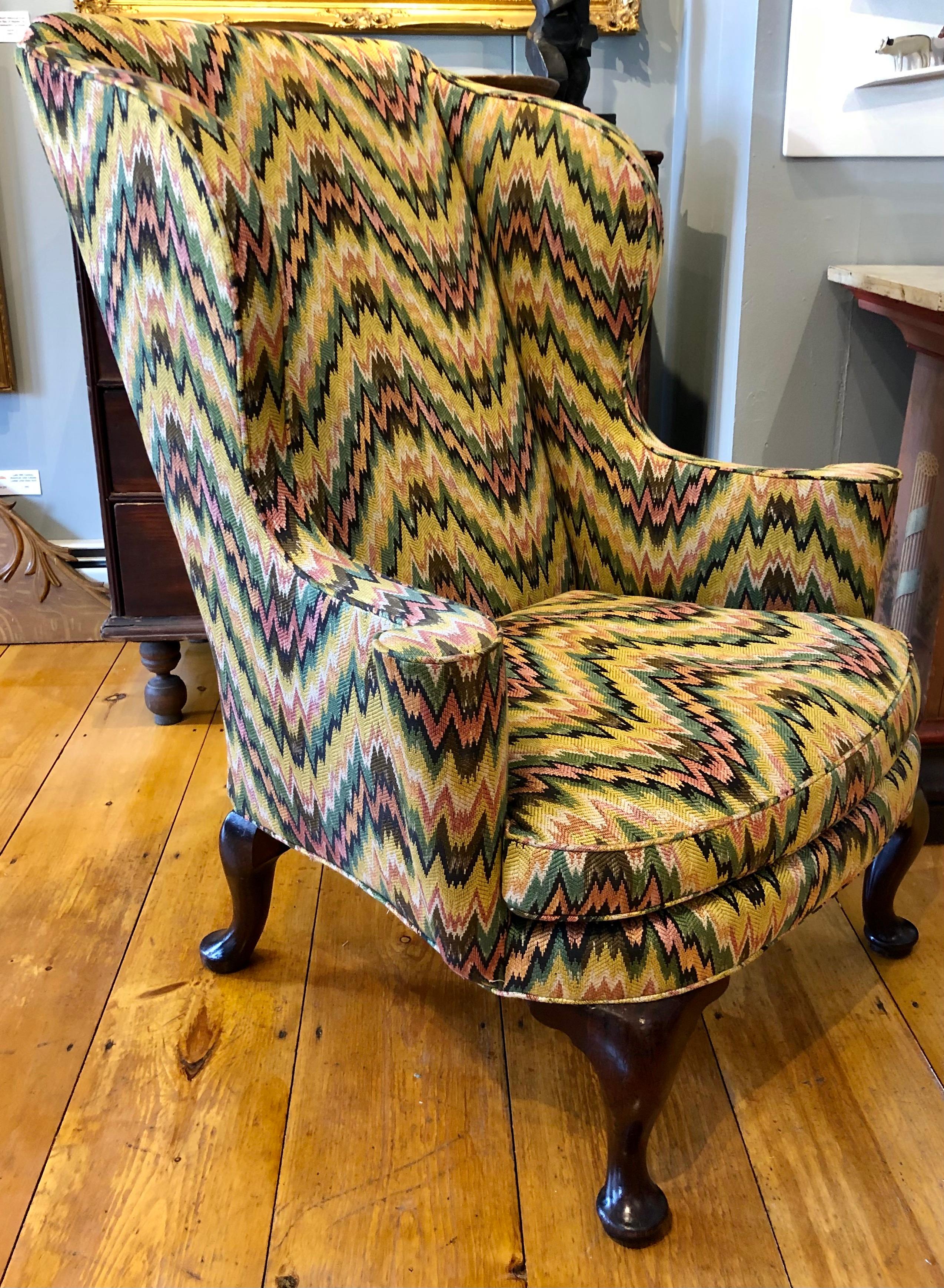 Queen Anne wing chair having rolled out arms with cones and re-upholstered in flame stitch fabric, all set on 4 cabriole legs ending in pad feet, circa mid-18th century. Most likely American, but could be English.

