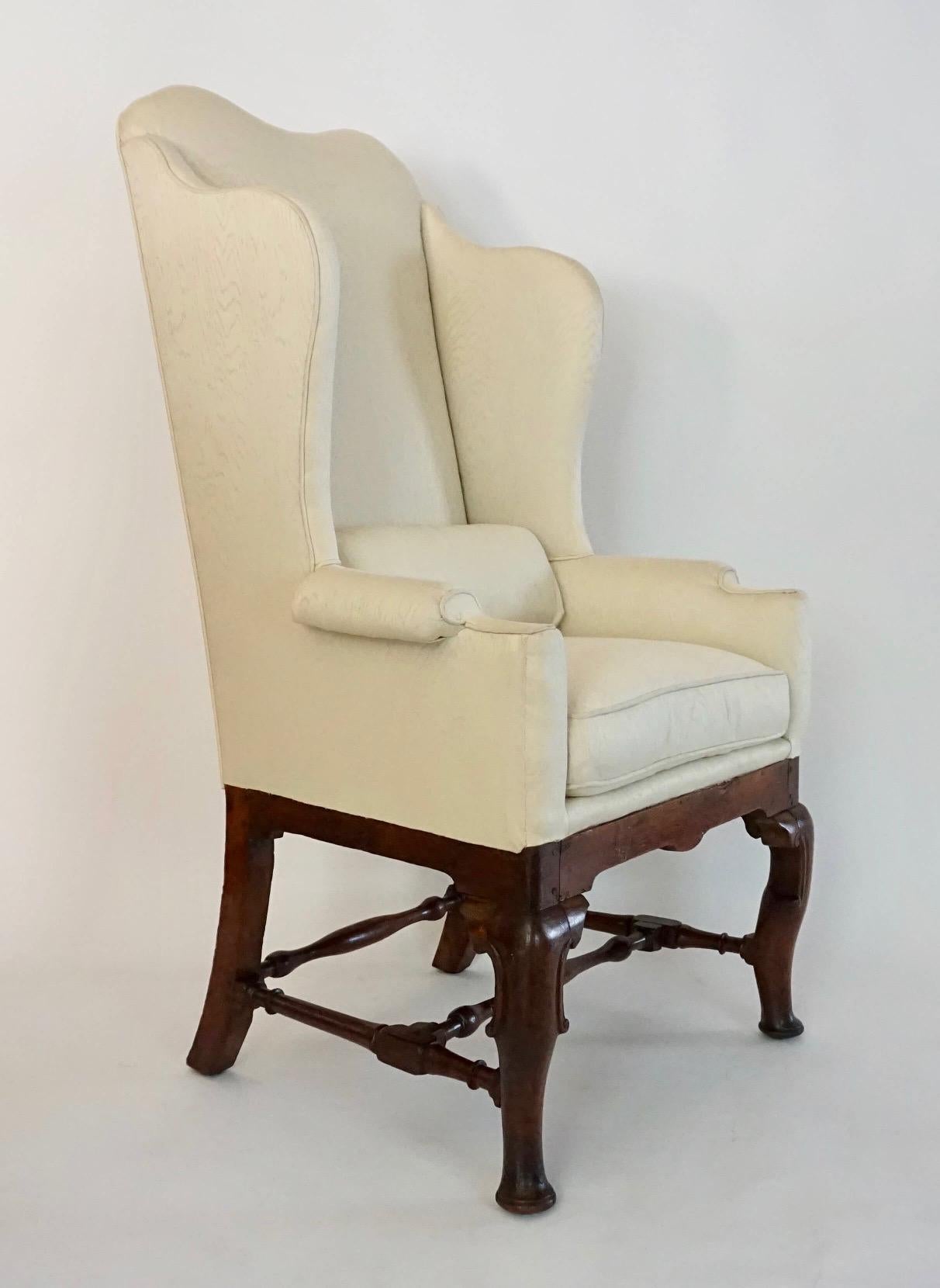 English early Queen Anne period wingback armchair of rare form having upholstered 'double-dome' top back-rail with sloped flanking wings connecting box-form arms with padded-rests either side loose down-filled cushion seat on carved oak base with