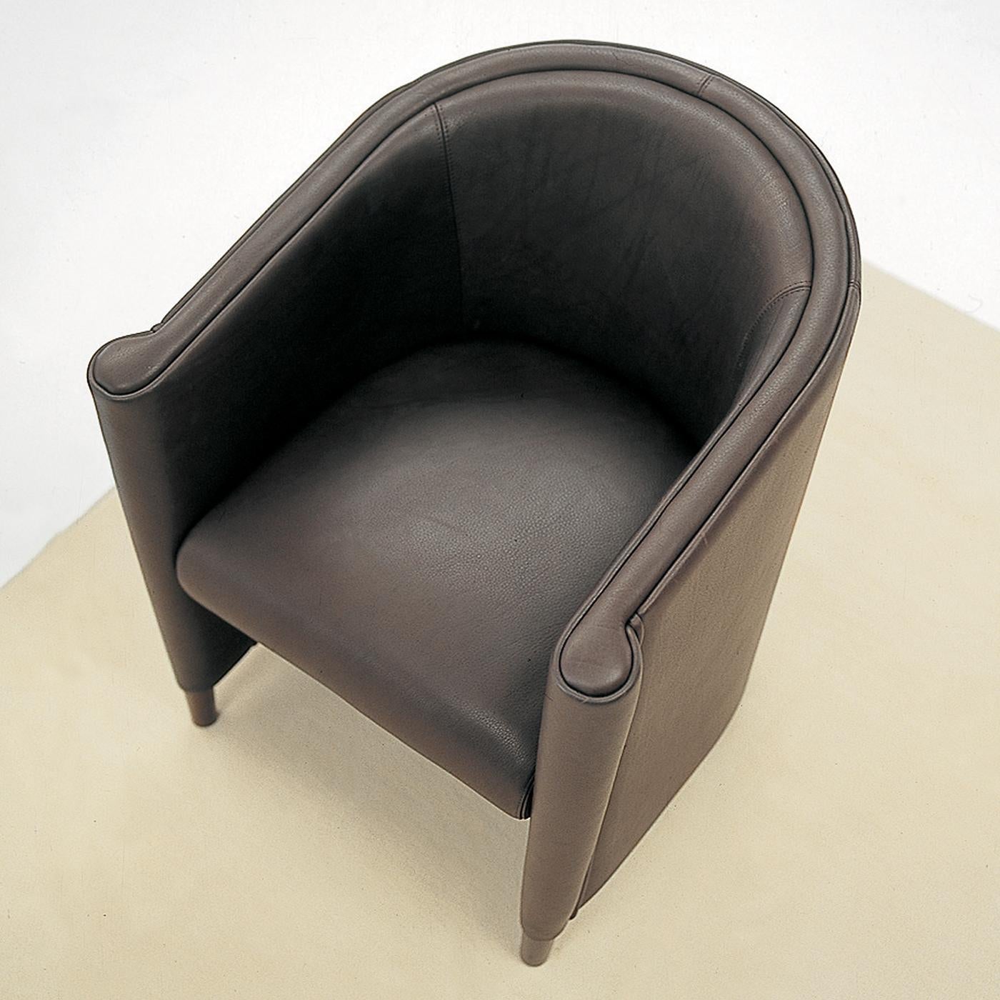 This dark-brown leather armchair is both sleek and cozy. Its enveloping, wraparound structure is like a cocooning nest, while its Minimalist shape is comprised of rounded forms and straight lines, creating a geometric structure that exudes personal