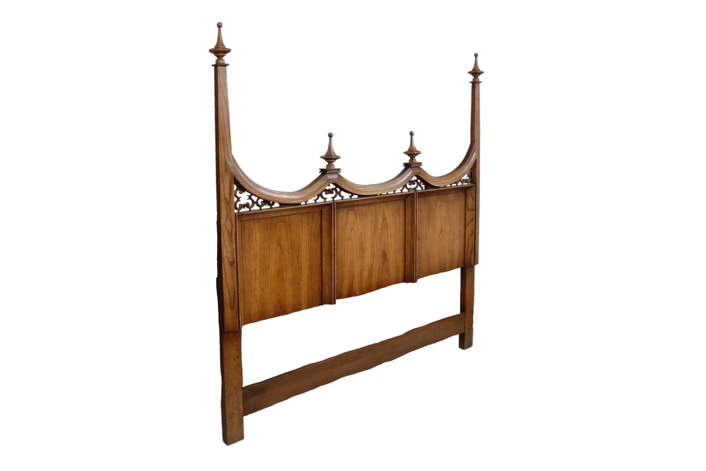 A Queen size neoclassical style headboard made of oak. The curved crest rail has four carved finials and is supported with decorative c-scrolls. Beveled cornices decorate three panels below.
