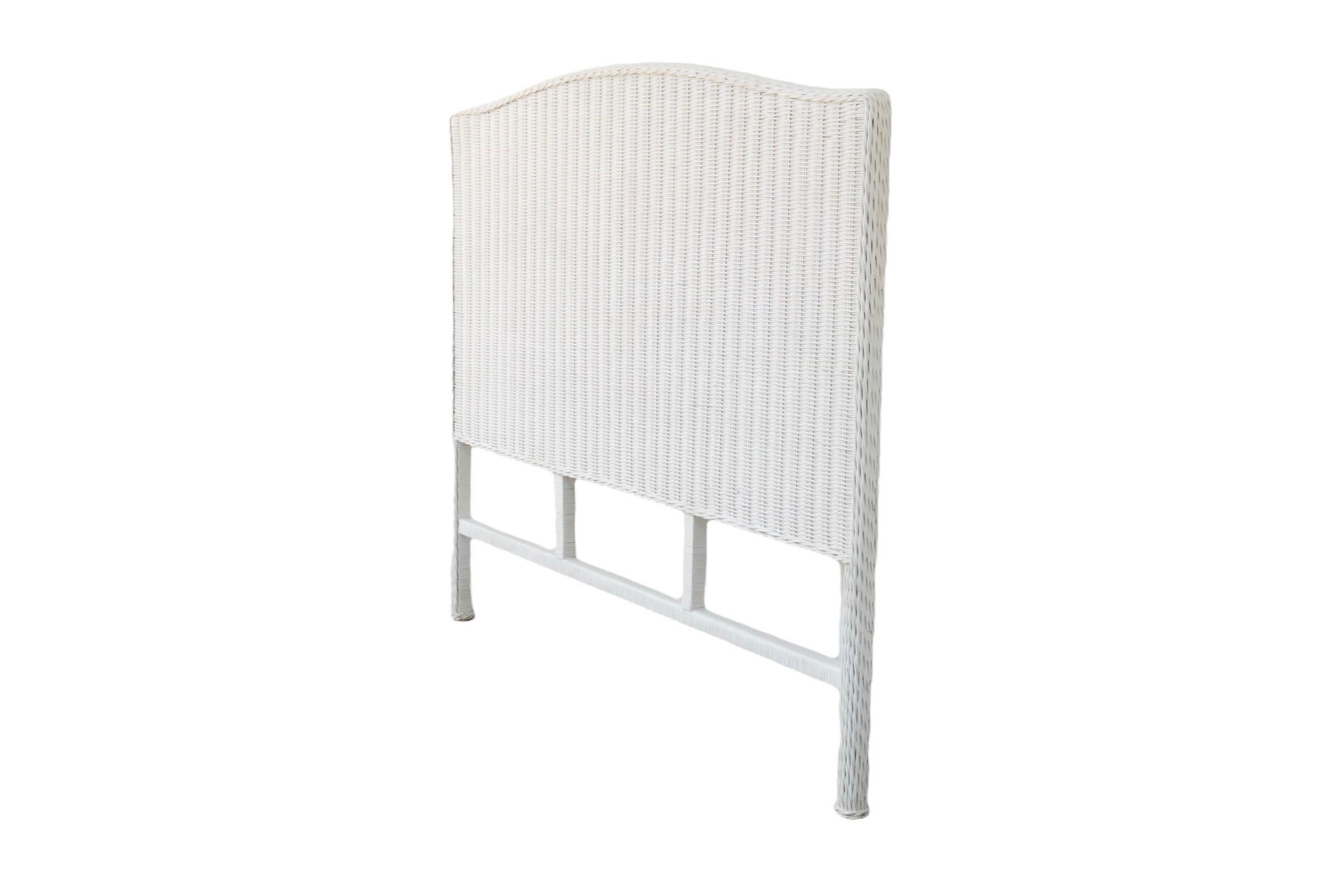A woven Queen size white wicker headboard. Squarish with a gentle camel shaped crest rail, finished with a thick braided trim that extends down rattan wrapped legs.

