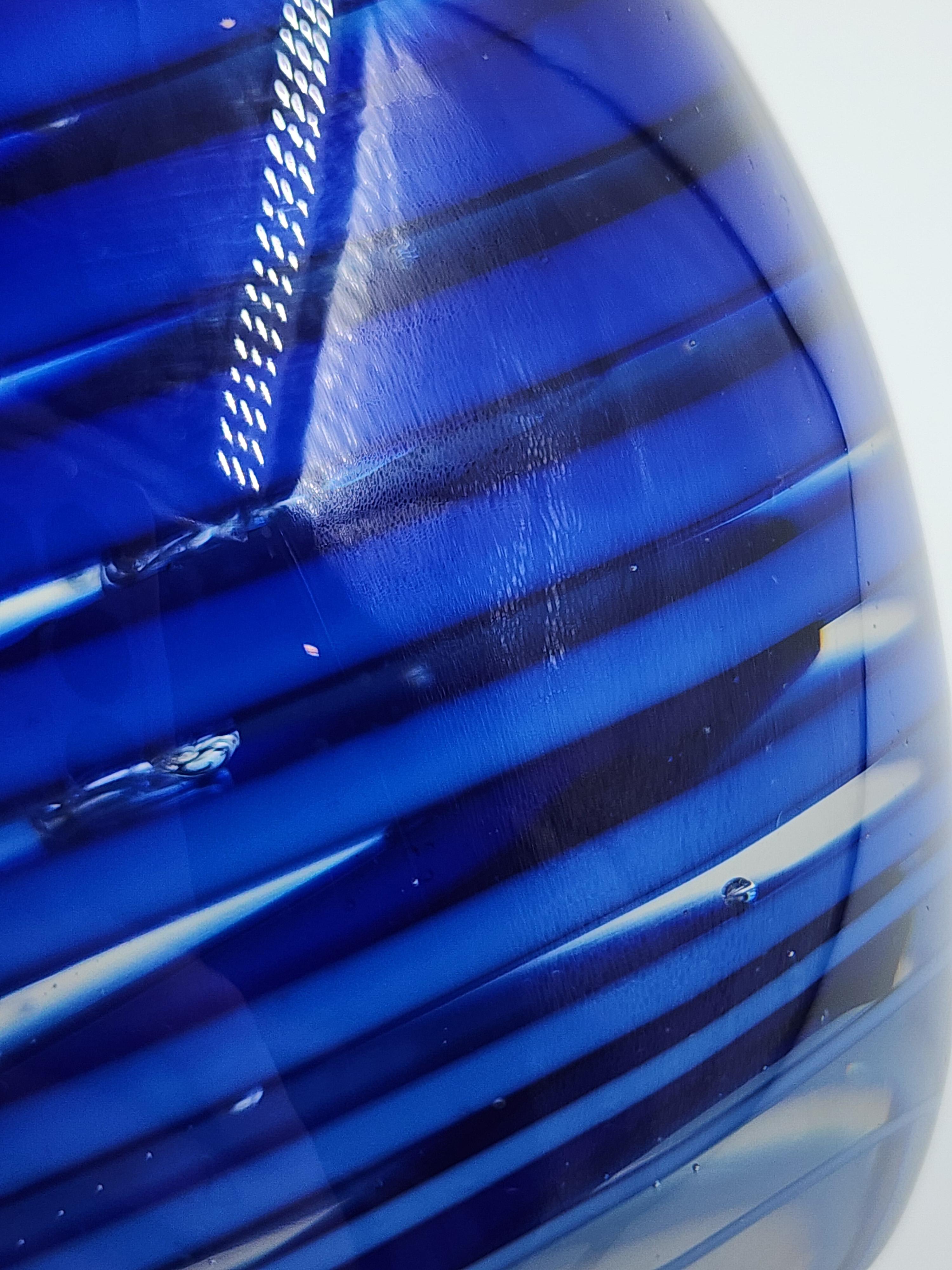Querandi Art Glass fermacarte in blu cobalto
Questo fermacarte in vetro artistico di Querandi ha una forma ovoidale. Il suo design è caratterizzato da un motivo di bande concentriche nei toni del blu cobalto, che ruotano verso il centro, creando un