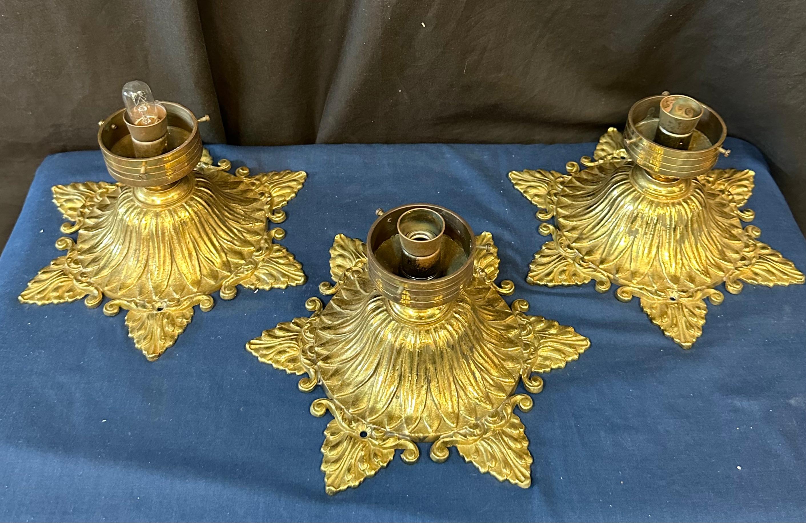 This interesting group of three vintage bronze flush mount ceiling fixtures dates from the 1920’s. Each sculptured bronze fixture features stylish decoration & holds a beautiful bell shape signed Quezal vibrant iridescent gold ribbed art glass lamp