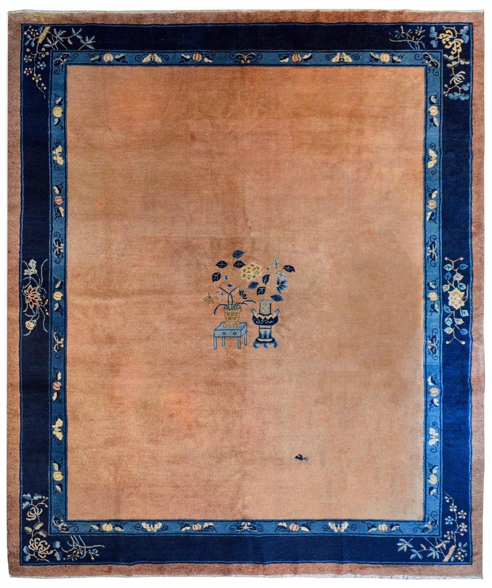 A quiet by chic early 20th century Chinese Feti rug with a simple medallion with a vignette containing a potted peony on a short table next to a tall vase with potted lotus, all on a solid salmon colored field and surrounded by a wide border