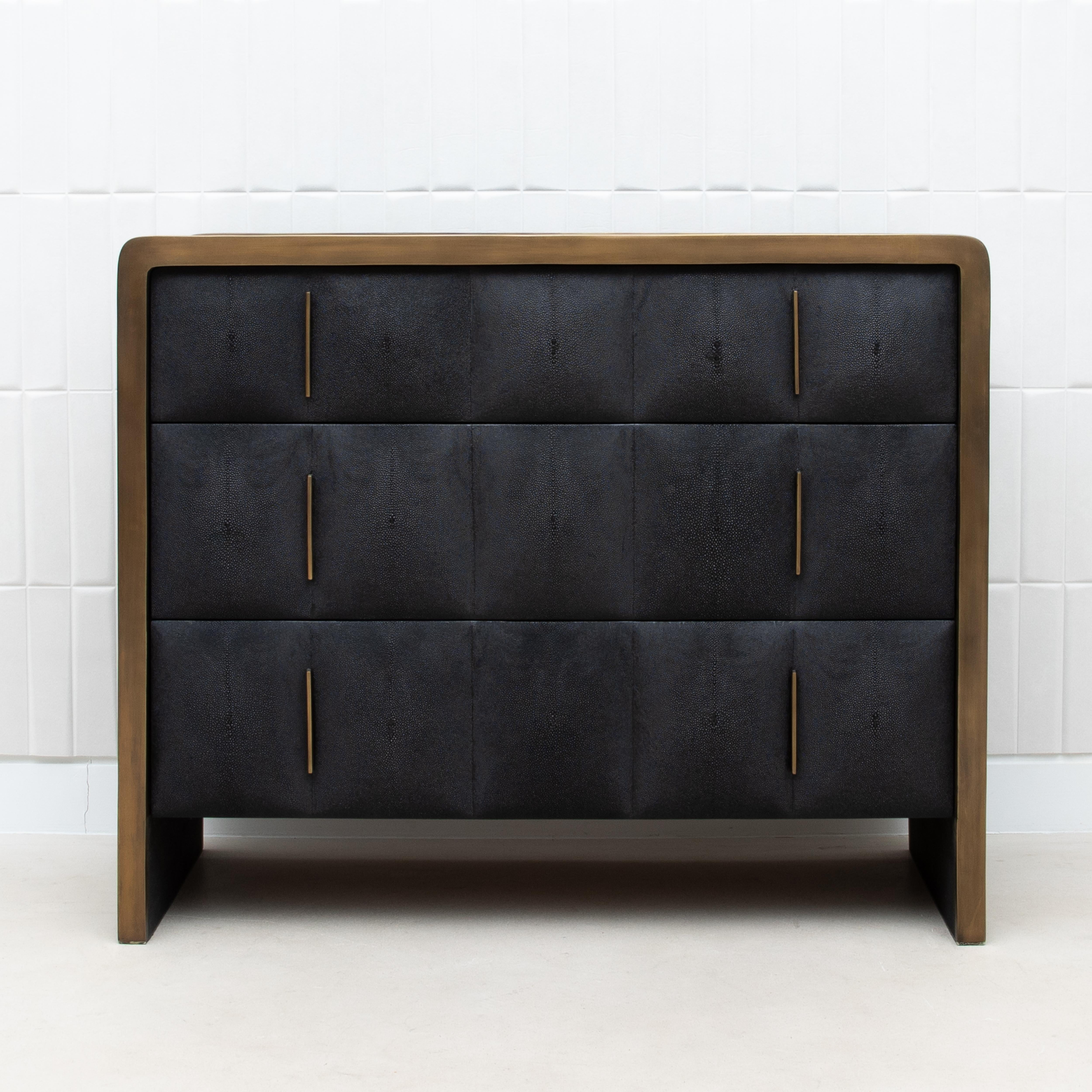 La commode Coco de R&Y Eleg est une déclaration de luxe discret, où l'élégance tactile du galuchat matelassé rencontre la richesse du laiton patiné bronze. Les tiroirs méticuleusement fabriqués à la main dégagent une impression d'opulence raffinée,
