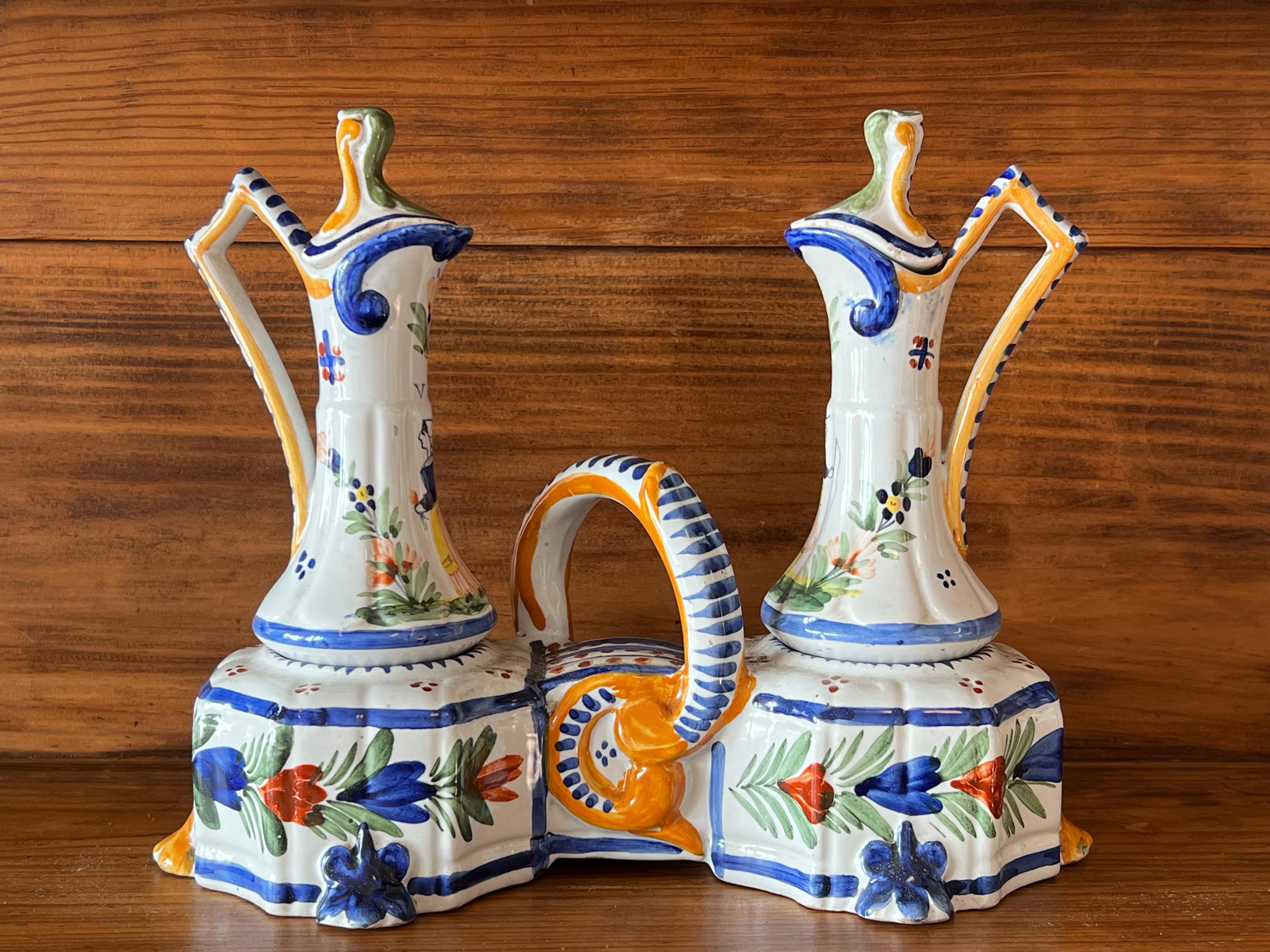 Late 19th century to early 20th century Quimper earthenware oil and vinegar set, signed HB Quimper manufacture located in Brittany, France. 
It consists of a stand, two small carafes with two lids, all made of earthenware with handmade decoration.