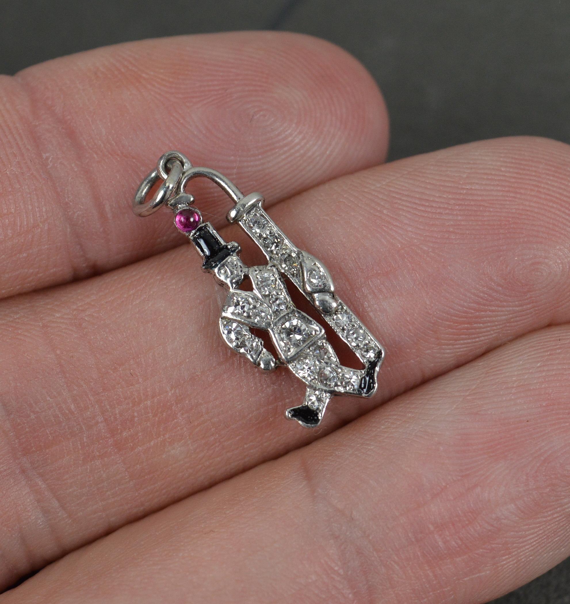 A fantastic Art Deco period pendant / charm. Circa 1920/30.
Solid platinum example.
Designed as a male in top hat with a lamp or lantern to side.
Set with a ruby cabochon to top, black enamel below and encrusted with many natural