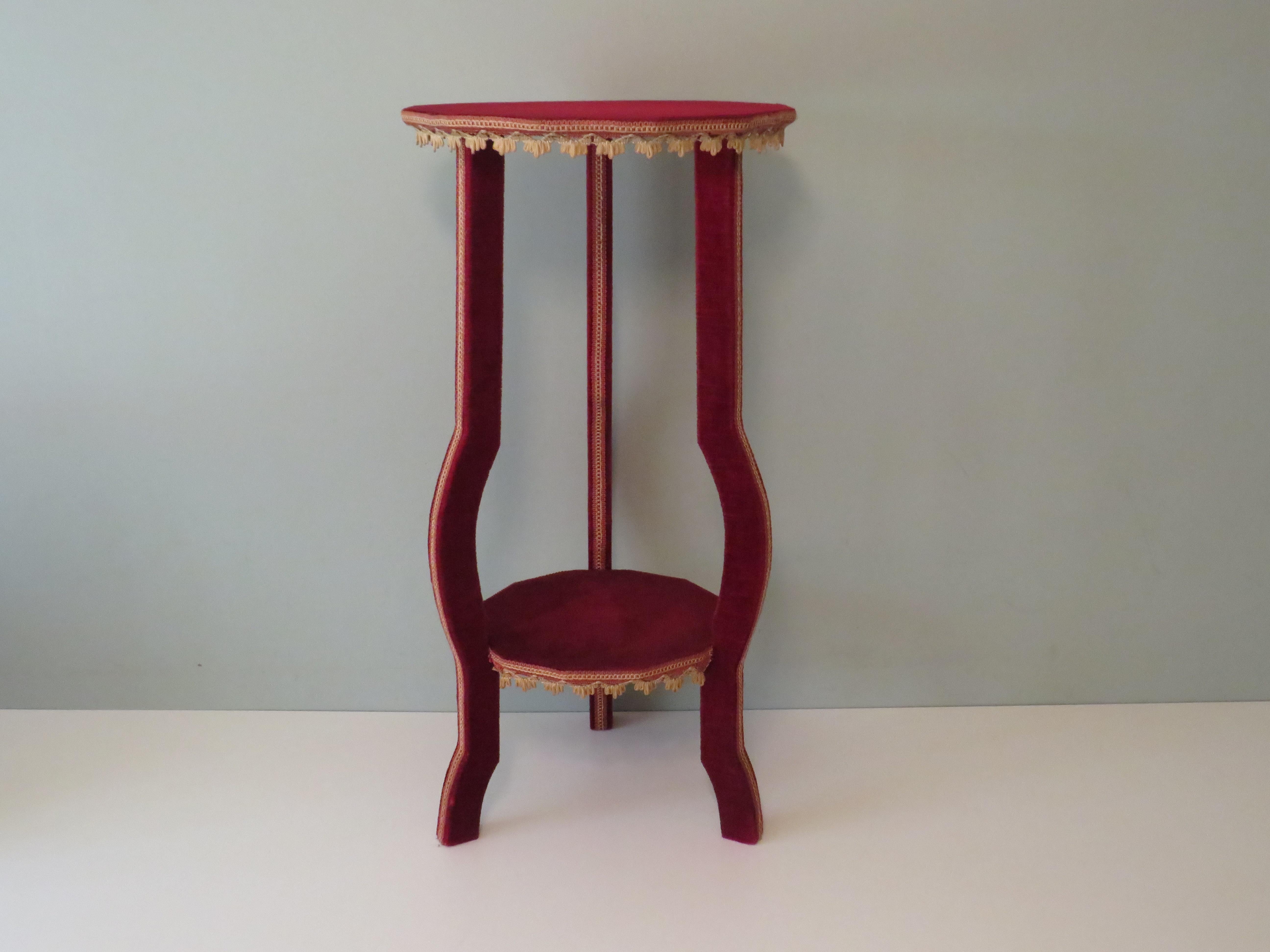 The table has a wooden frame that is covered with dark red velvet and finished with dark pink and gold-coloured piping. The underside of the table tops is covered with dark red moiré fabric.
The table has two 12-sided table tops. The lowest table
