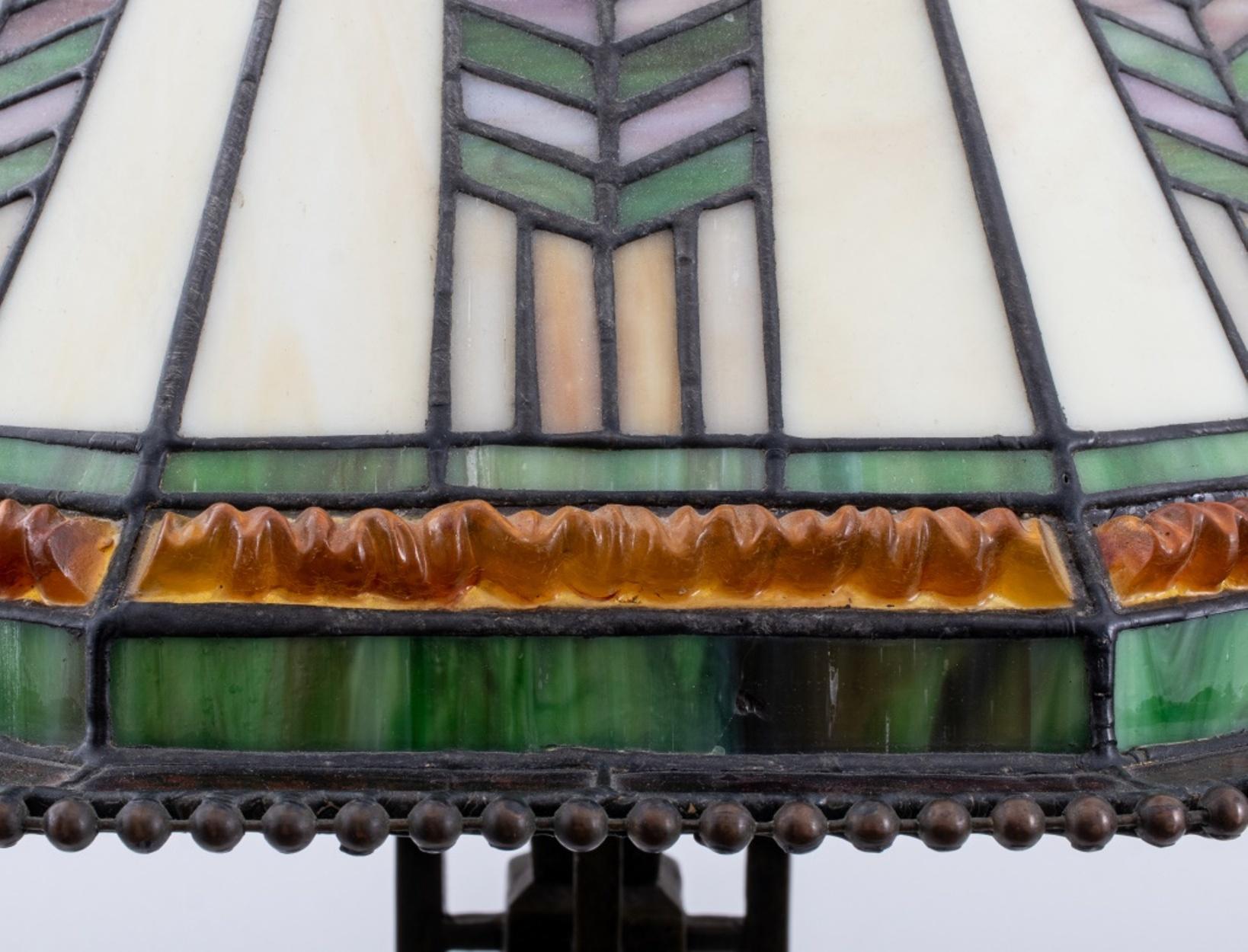 Tiffany manner slag glass table lamp, the shade with orange, purple, and green geometric design, the bronzed composite base with Prairie style geometric buttresses in the manner of Frank Lloyd Wright (American, 1867-1959).

Dimensions: 28