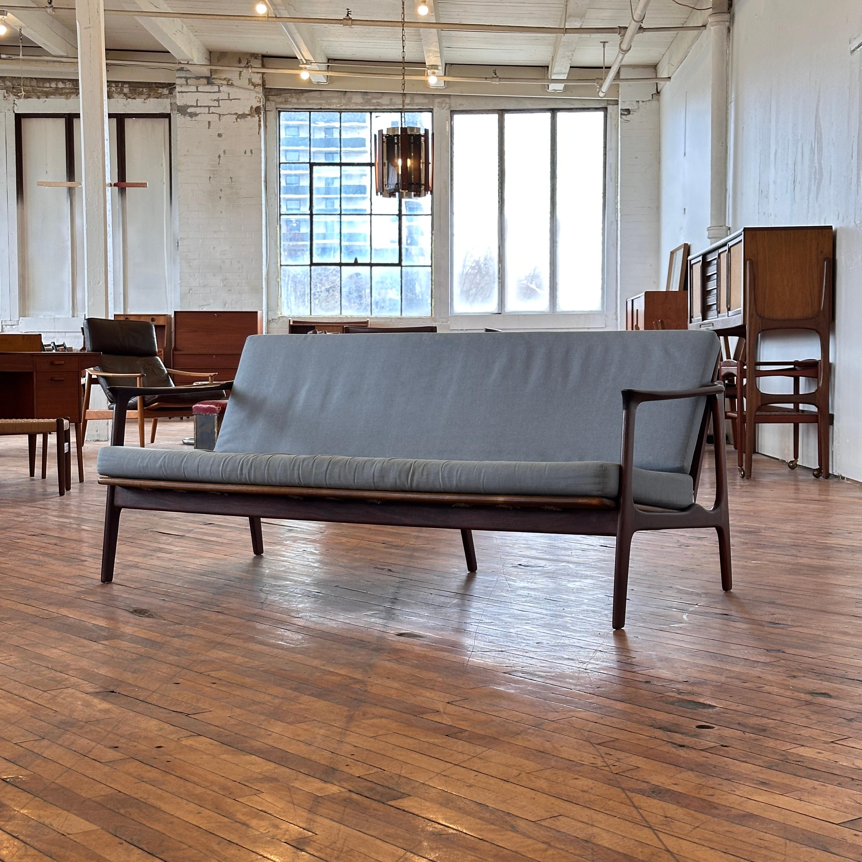 Exuding timeless Scandinavian design, this exceptional three-seater sofa by R. Huber & Co. showcases the finest craftsmanship of mid-century modern furniture. Constructed from rich, solid teak, the frame boasts elegant, clean lines and a gently
