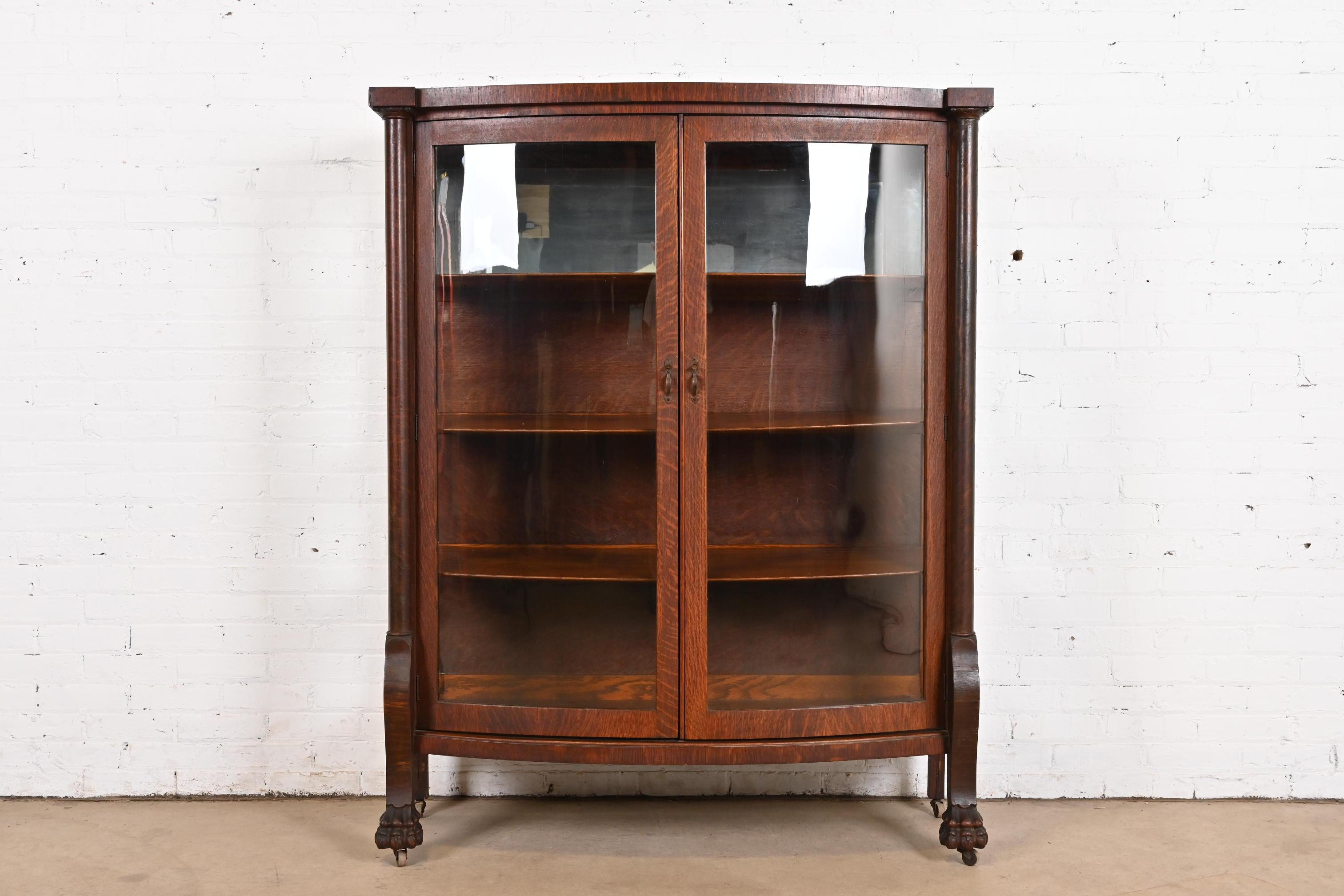 A beautiful antique American Empire or Victorian bow front bookcase or display cabinet

In the manner of R. J. Horner & Co.

USA, Circa 1890

Quarter sawn oak, with glass front and sides, mirrored back, carved lion's paw feet, and original brass