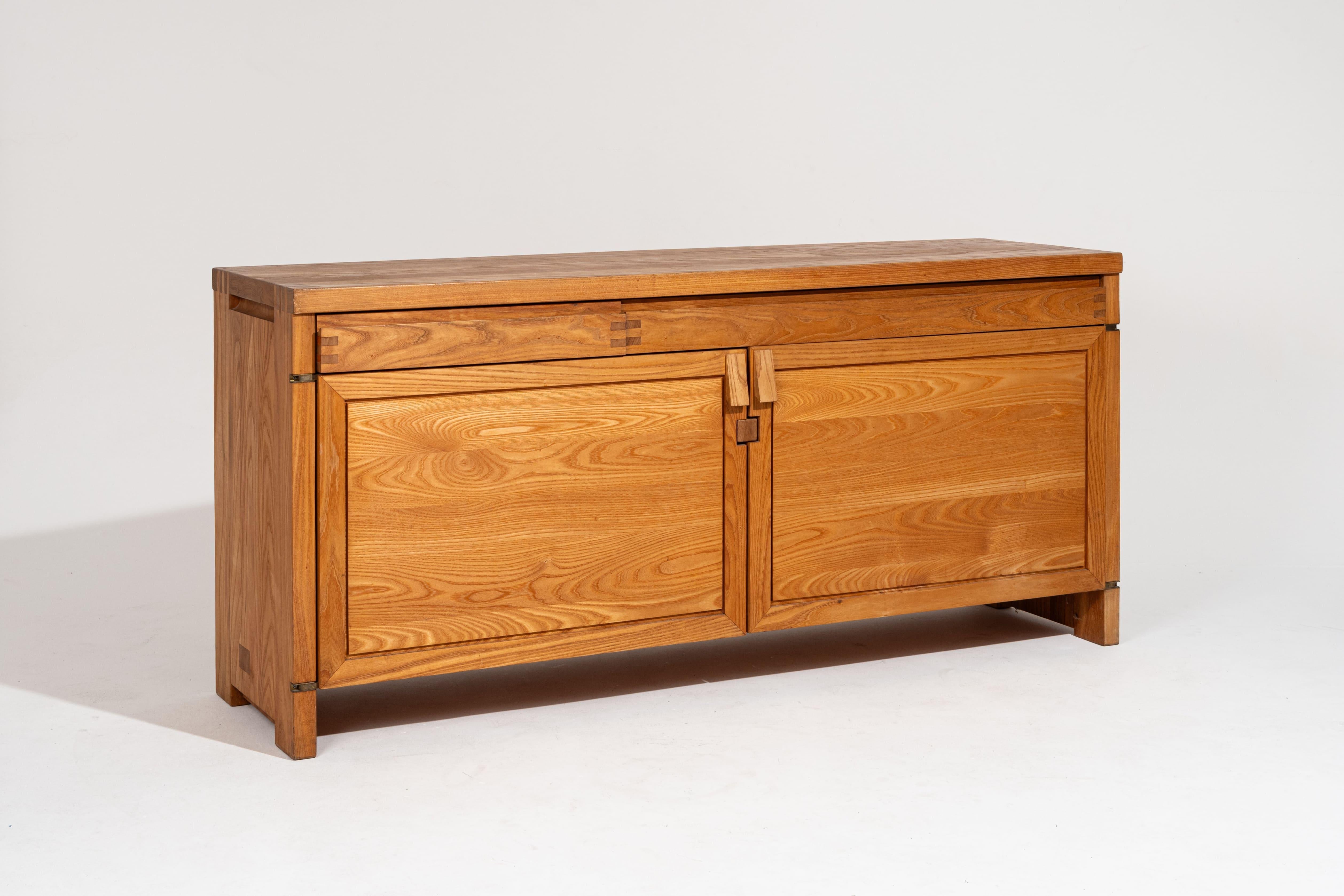 Credenza R08 in olmo massiccio, progettata dal designer e architetto d'interni francese Pierre Chapo (1927-1987) negli anni Sessanta. Presenta due ante a battente sormontate da due cassetti asimmetrici incastonati nel grembiule, che offrono un