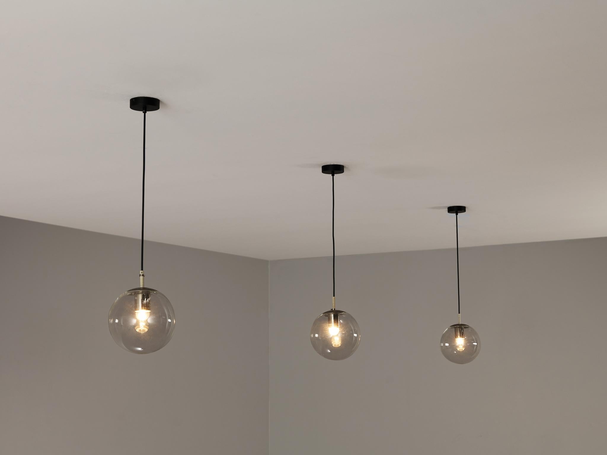 RAAK Amsterdam, pendants, glass, metal, Europe, 1970s.

This atmospheric set of pendant lamps features each a glass orb, casting a gentle and soothing light tone that imbues the space with a vibrant atmosphere. The lamps can be hung above a large